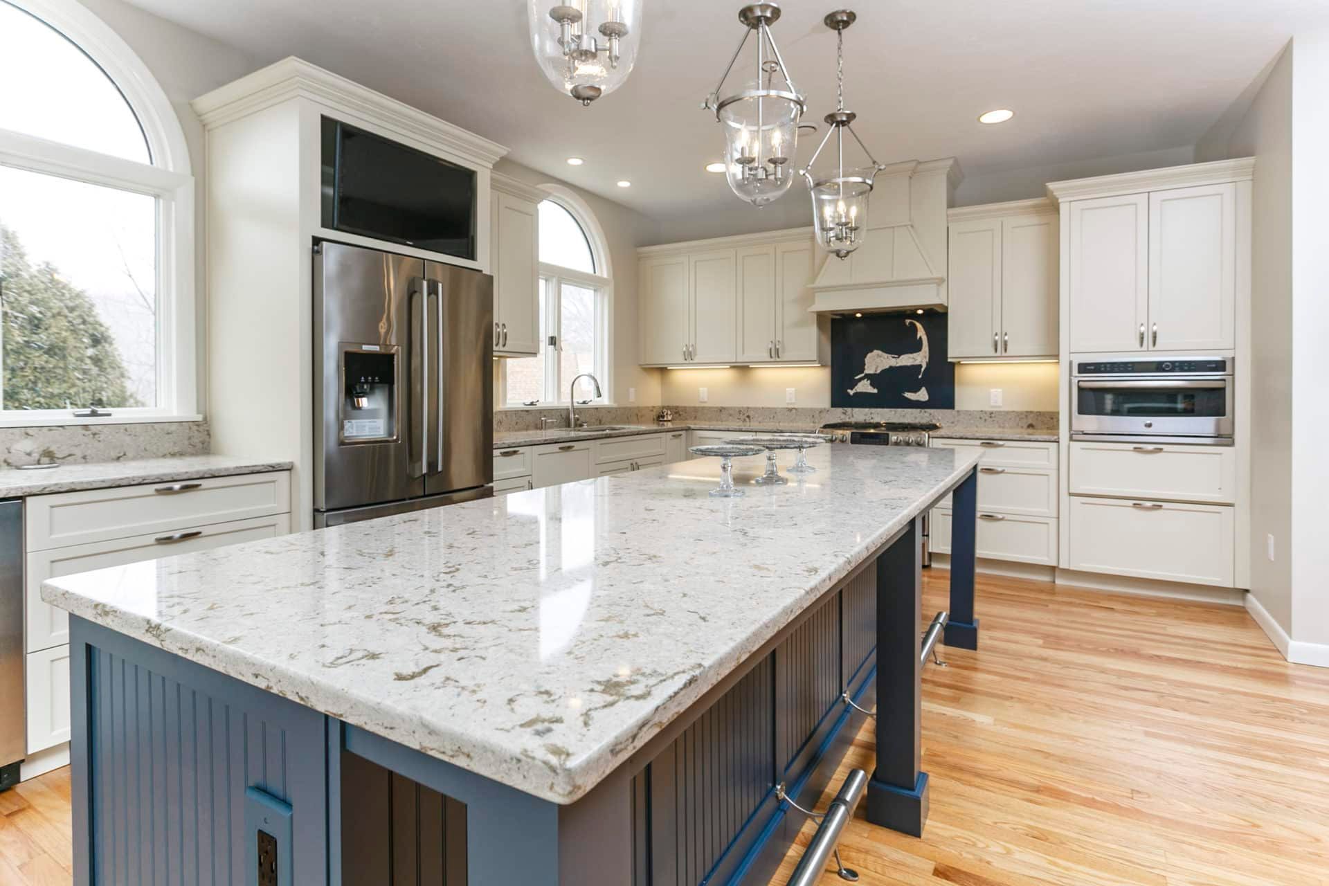 A kitchen with white cabinets, granite counter tops, stainless steel appliances, and a large island.
