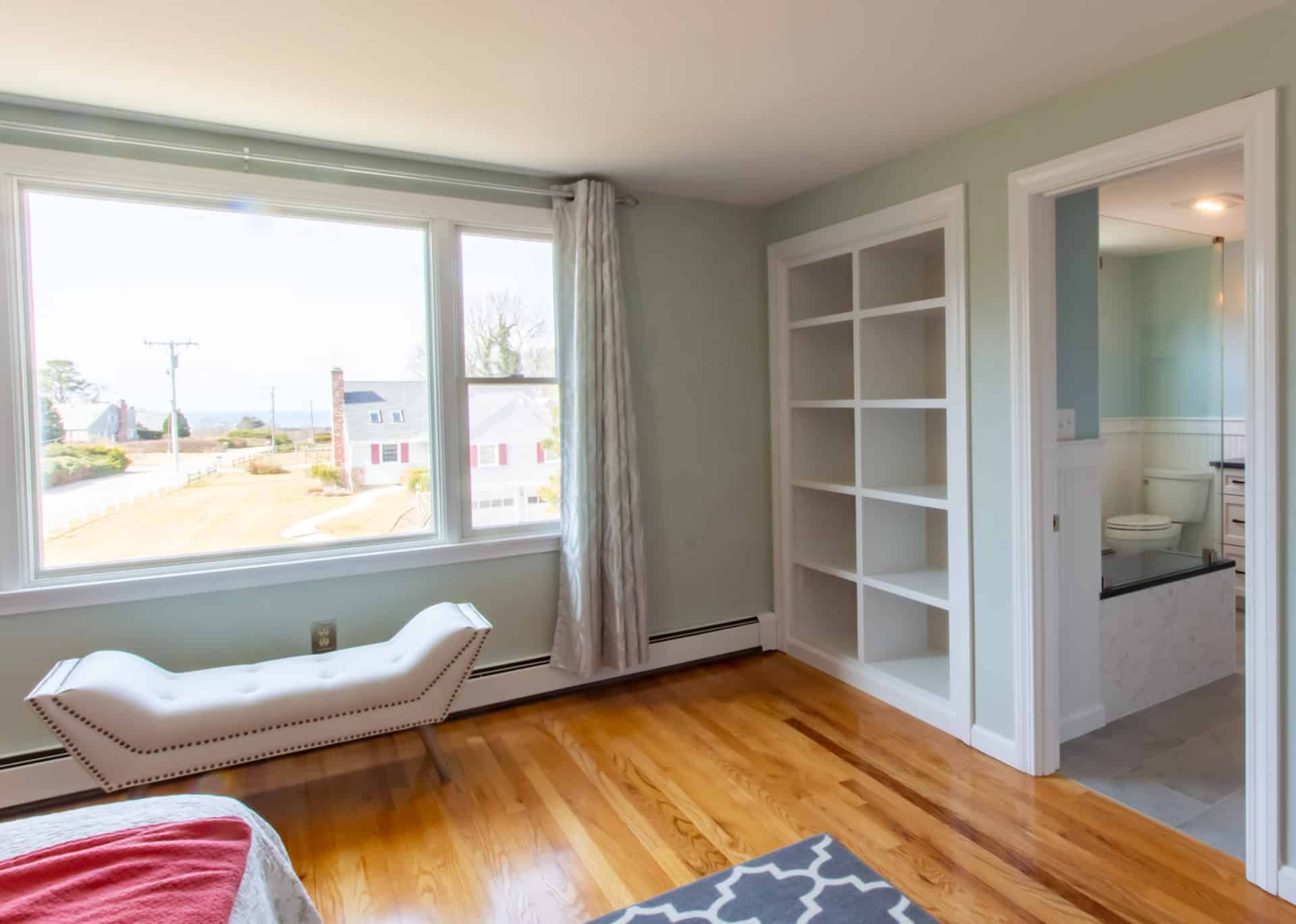 A bedroom with hardwood floors , a bed , a bench and a window.