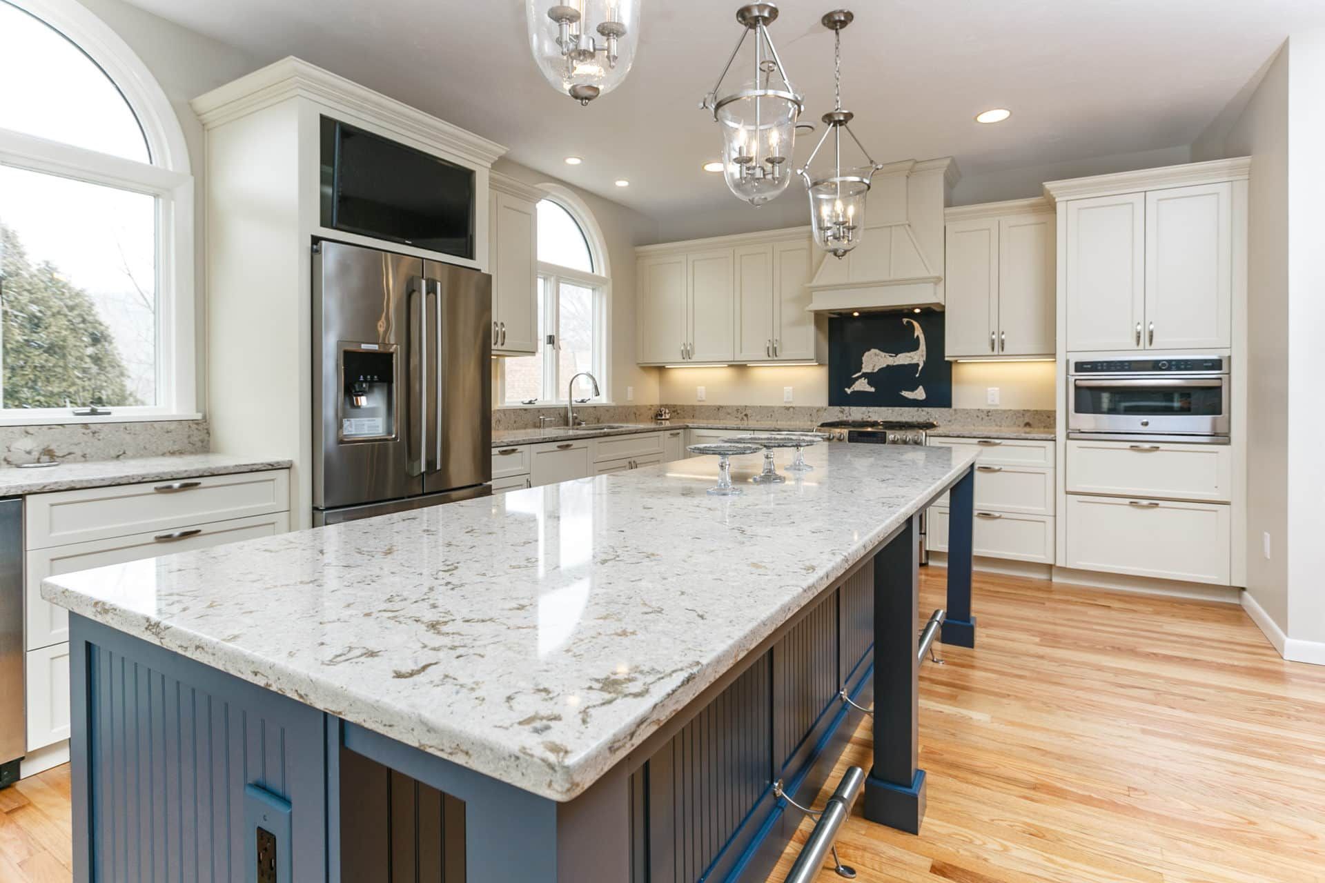 A kitchen with white cabinets, granite counter tops, stainless steel appliances and a large island.