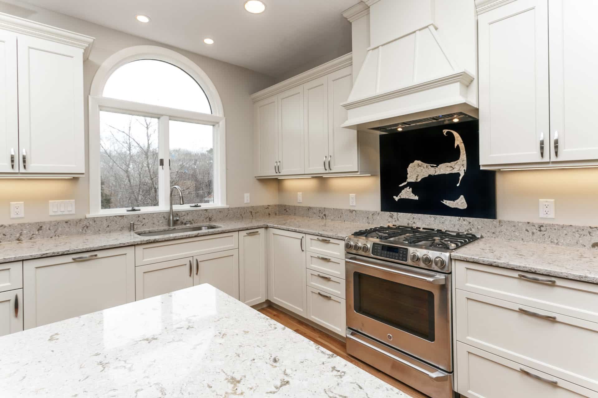 A kitchen with white cabinets, granite counter tops, stainless steel appliances and a large island.
