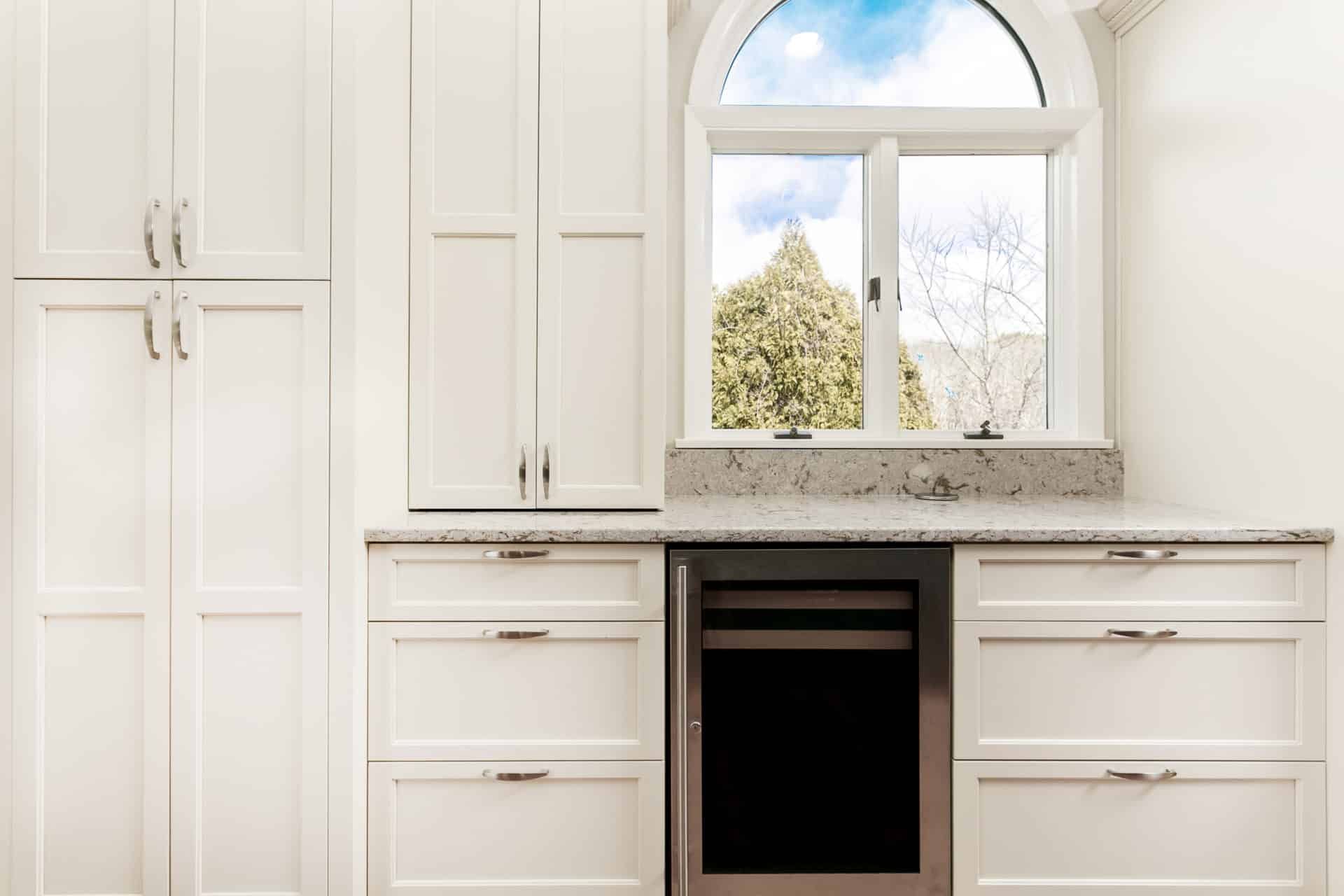 A kitchen with white cabinets, stainless steel appliances, and a large window.