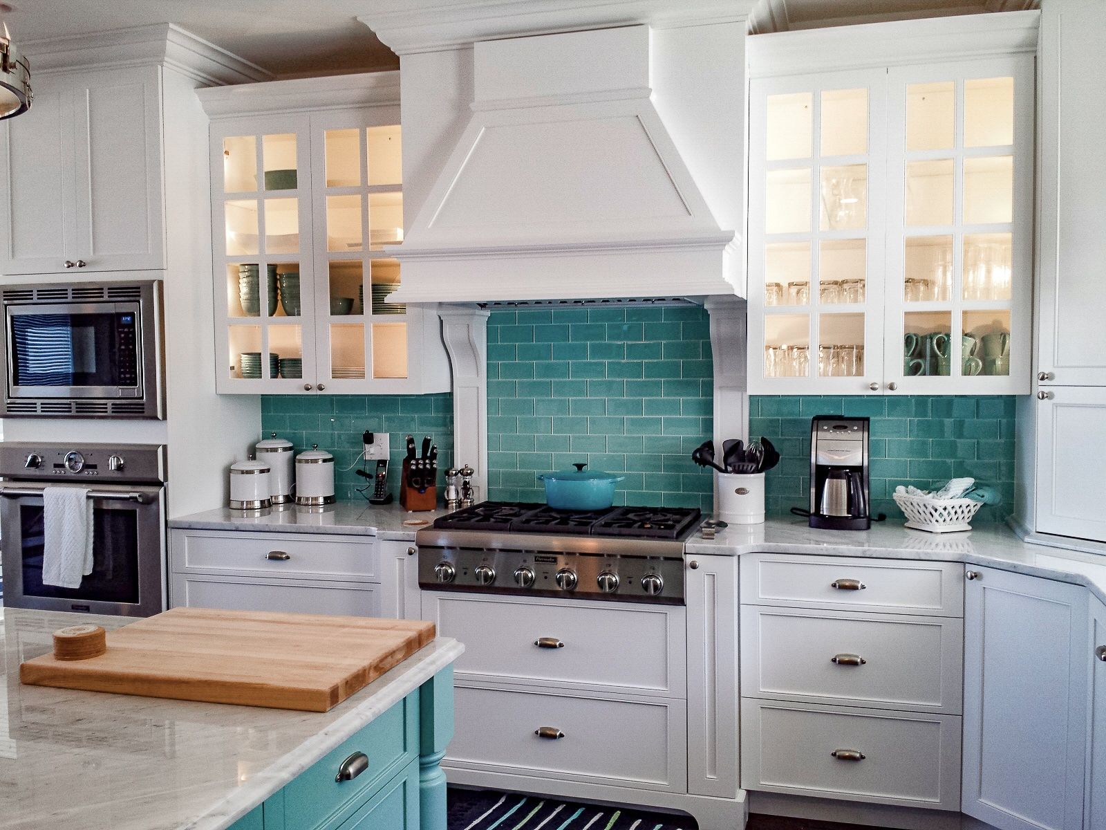 A kitchen with white cabinets, a stove, a microwave, and a cutting board.