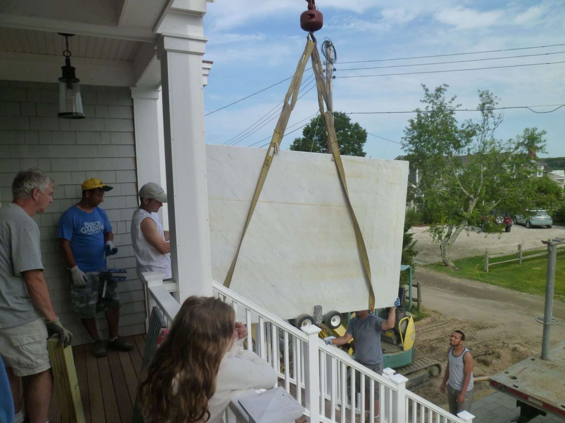 A group of people standing on a porch watching a crane lift something