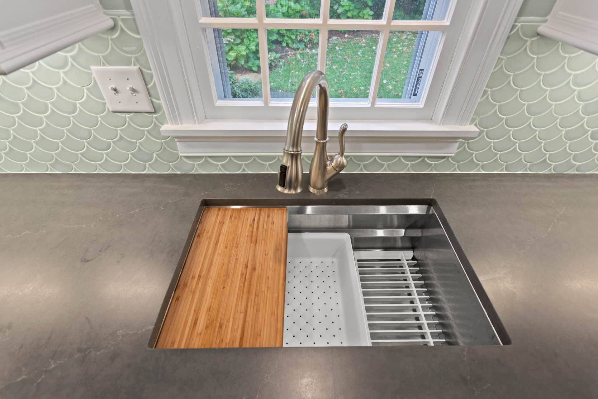 A kitchen sink with a wooden cutting board and a window.