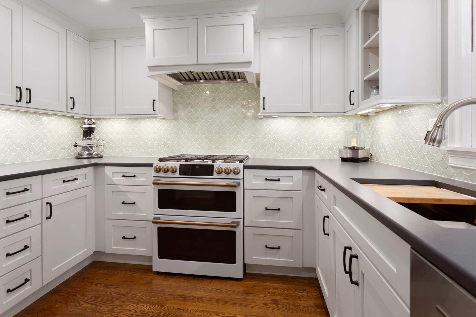 A kitchen with white cabinets, black counter tops, a stove and a sink.