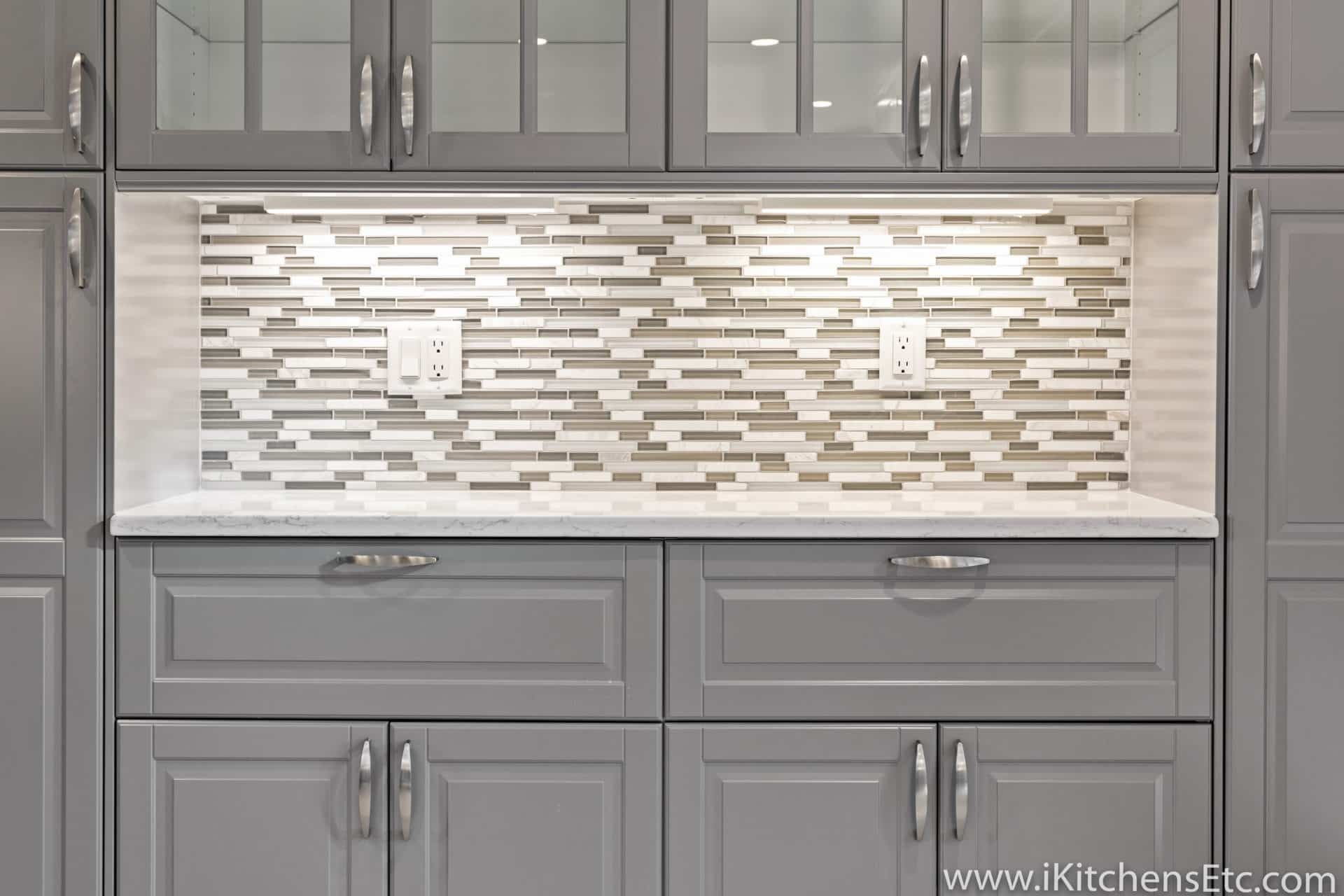 A kitchen with gray cabinets and a mosaic tile wall.