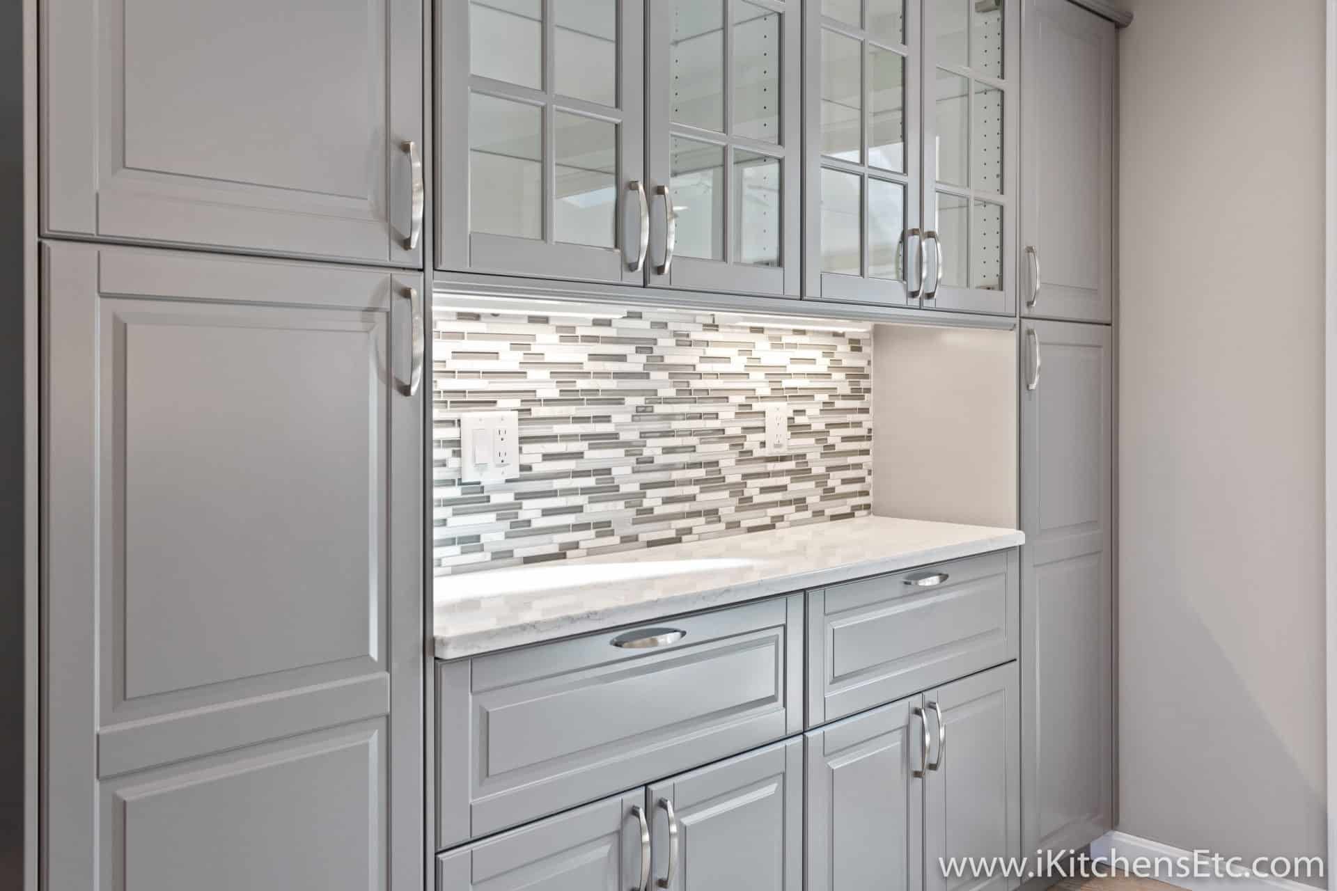 A kitchen with gray cabinets and white counter tops.
