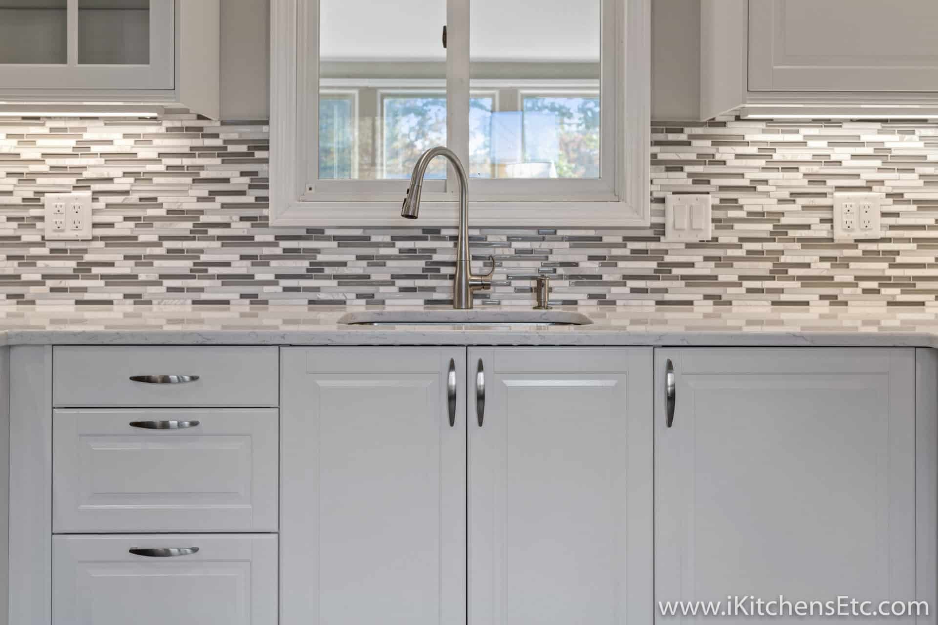 A kitchen with white cabinets and a sink with a window