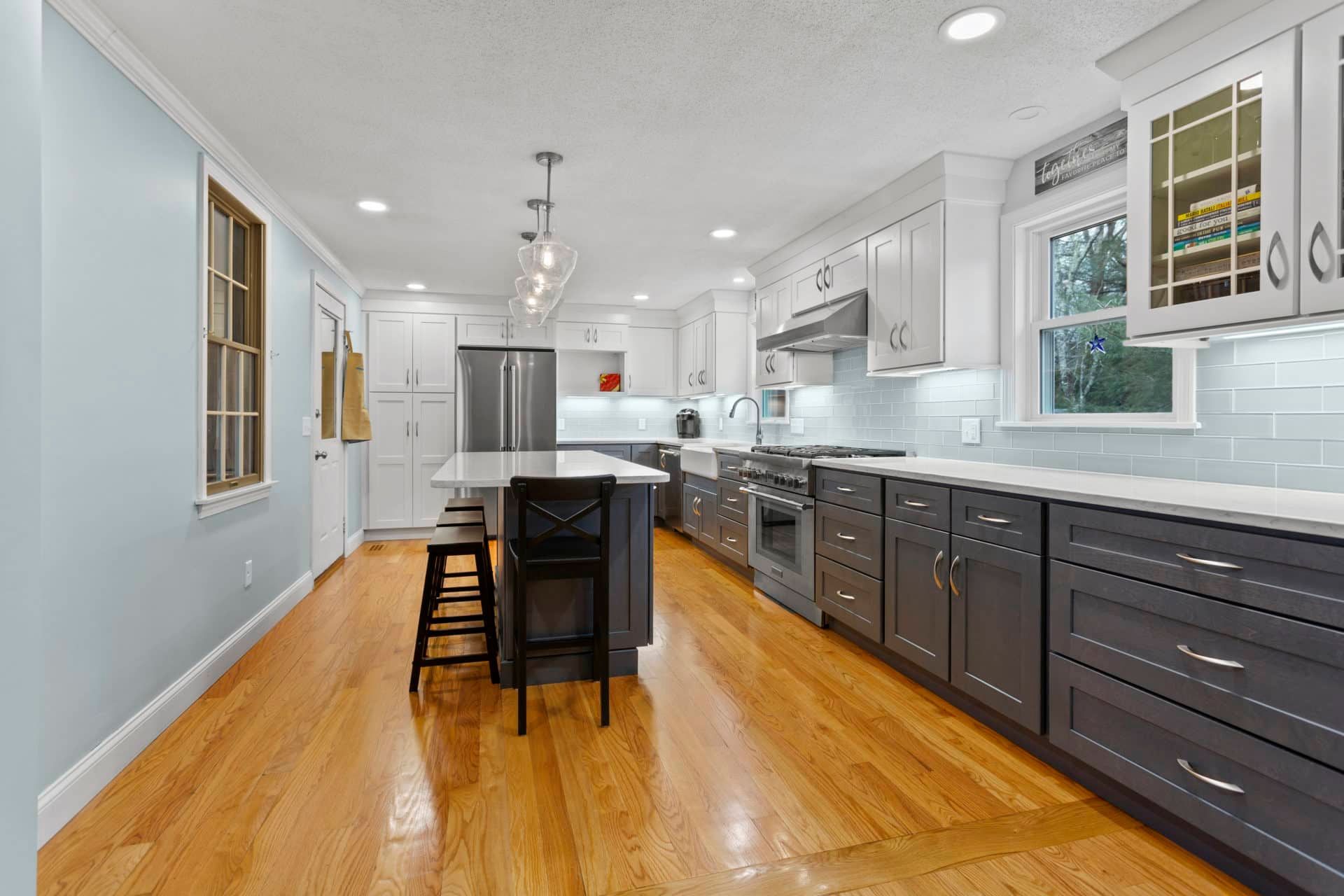 A kitchen with hardwood floors , gray cabinets , stainless steel appliances and a large island.