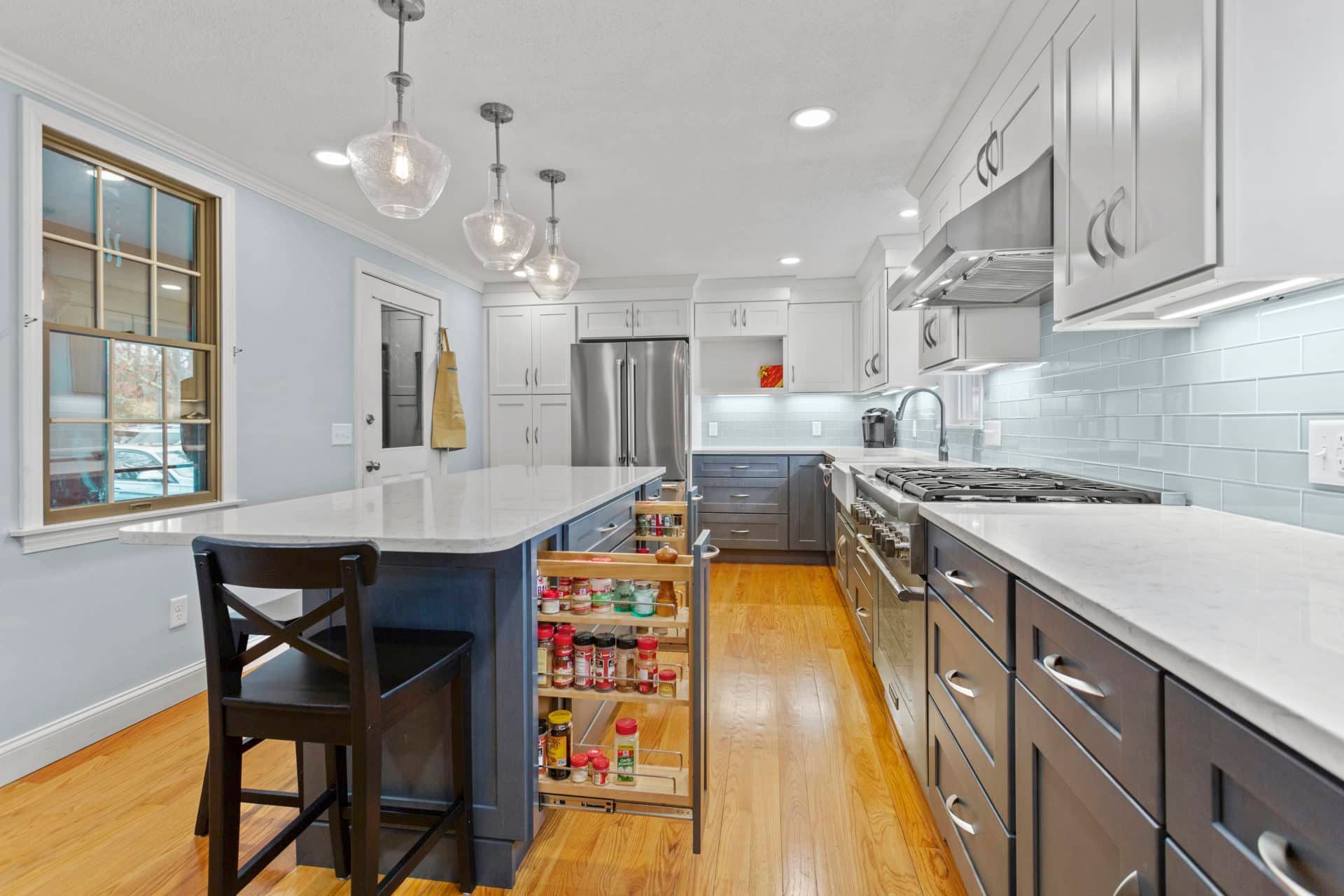 A kitchen with stainless steel appliances, gray cabinets, white counter tops and a large island.