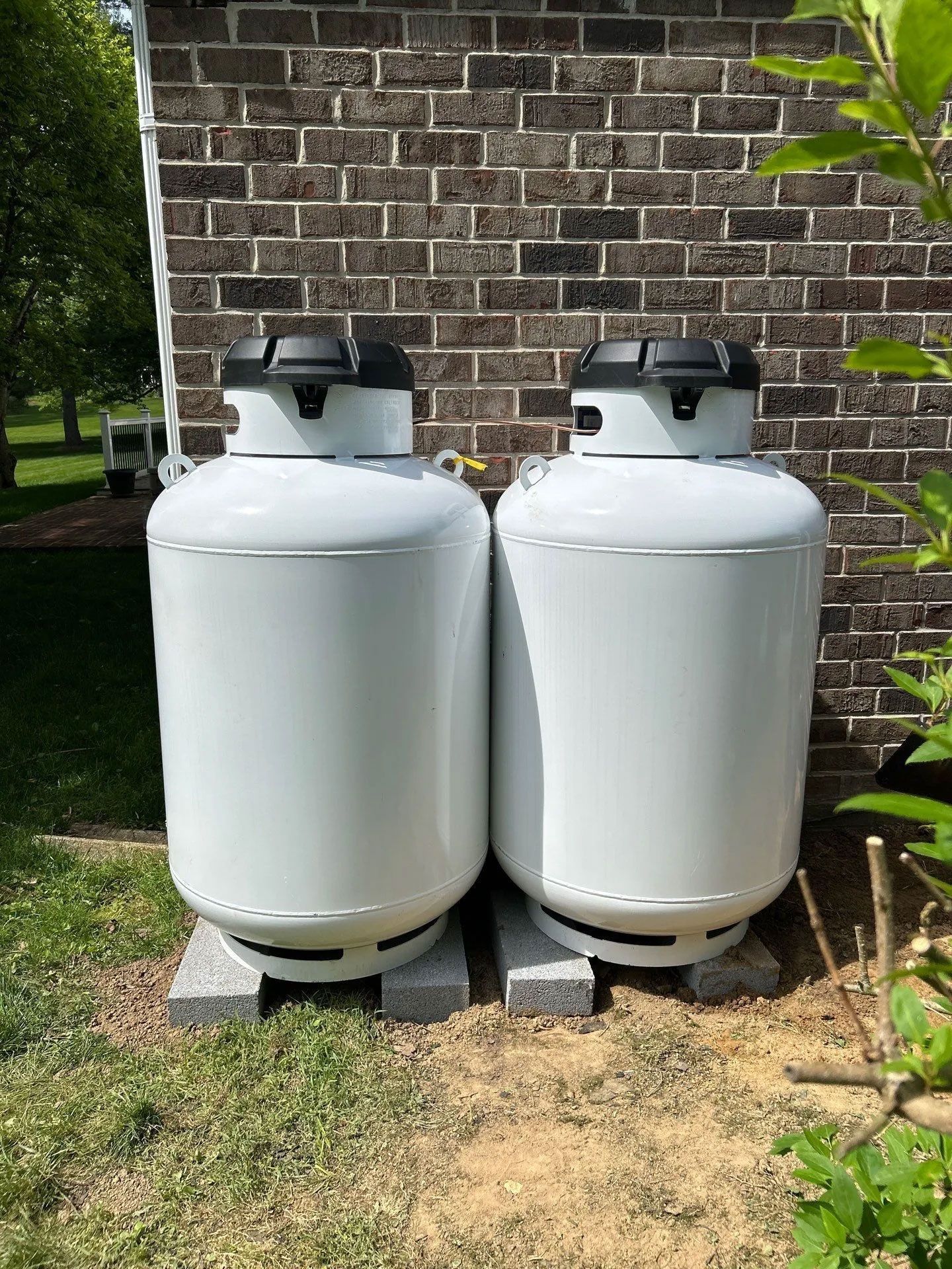 Two white propane tanks beside a brick house wall on a small concrete pad