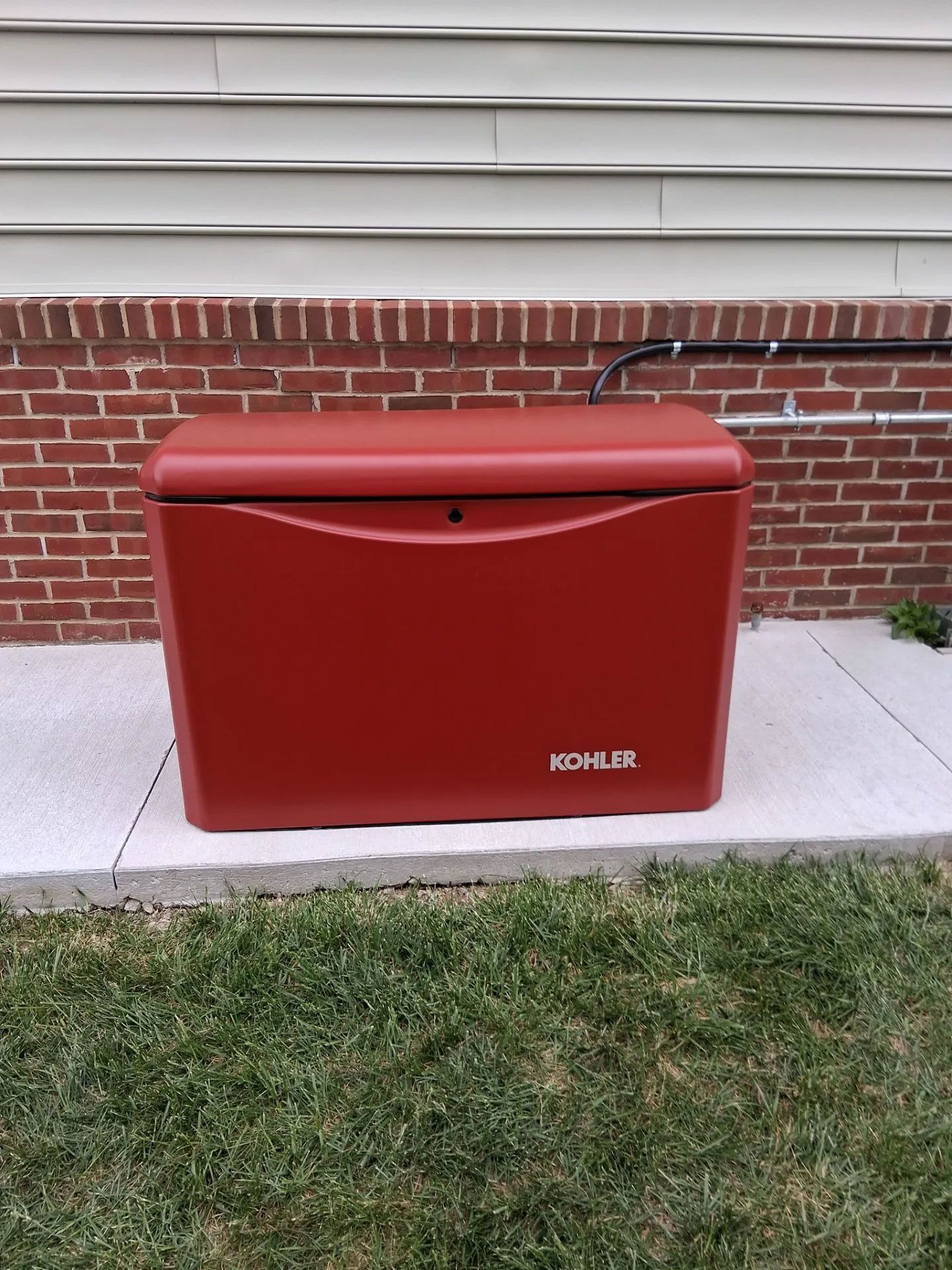 Red Kohler outdoor generator box against a brick house wall and grass lawn