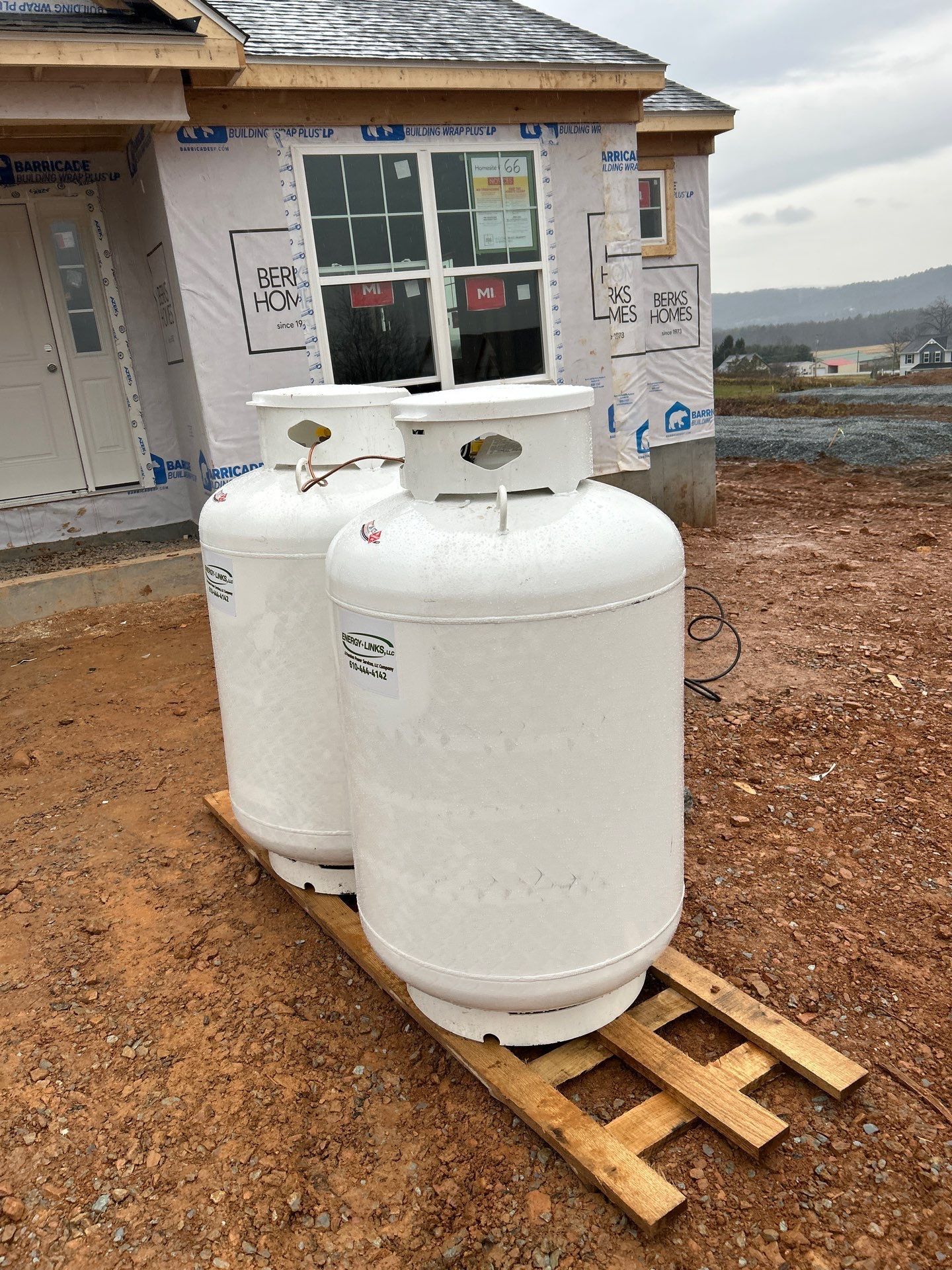 Two white propane tanks on a wooden pallet beside a house under construction.