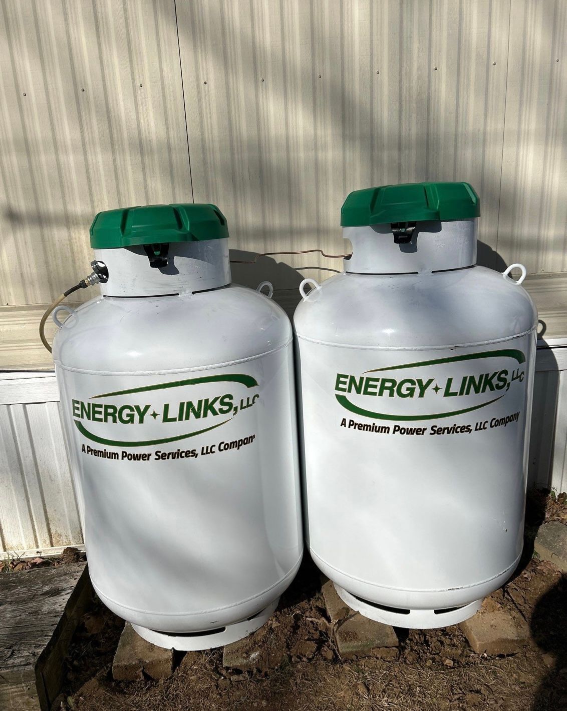 Two white Energy-Link LPG cylinders with green caps standing outdoors against a corrugated wall