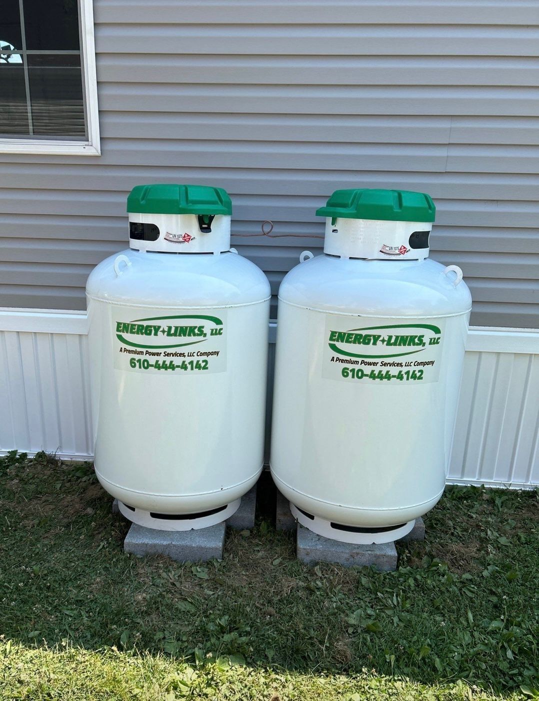 Two white water softener tanks with green lids standing outside against a gray house wall.