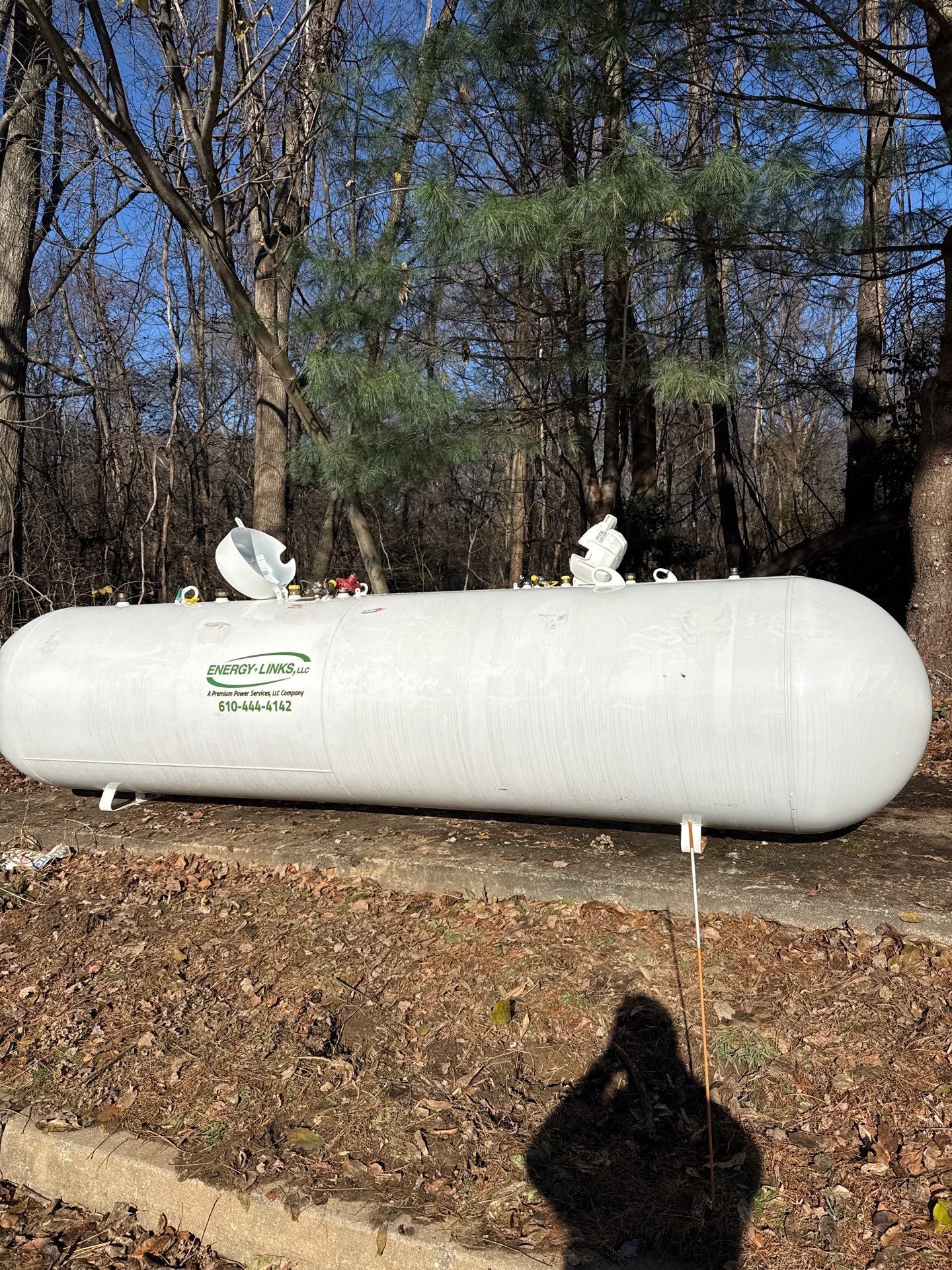 Large white propane tank in a wooded area with small snow patches on top