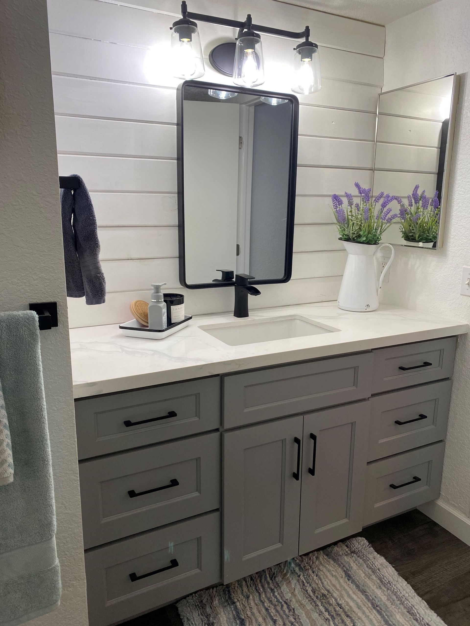 A bathroom with gray cabinets , a sink , and a mirror.