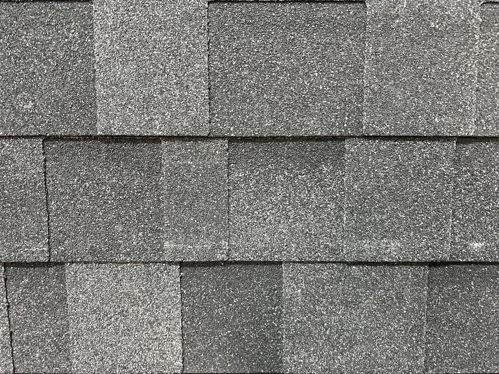 A close-up view of overlapping gray asphalt roof shingles with a varied, speckled texture.