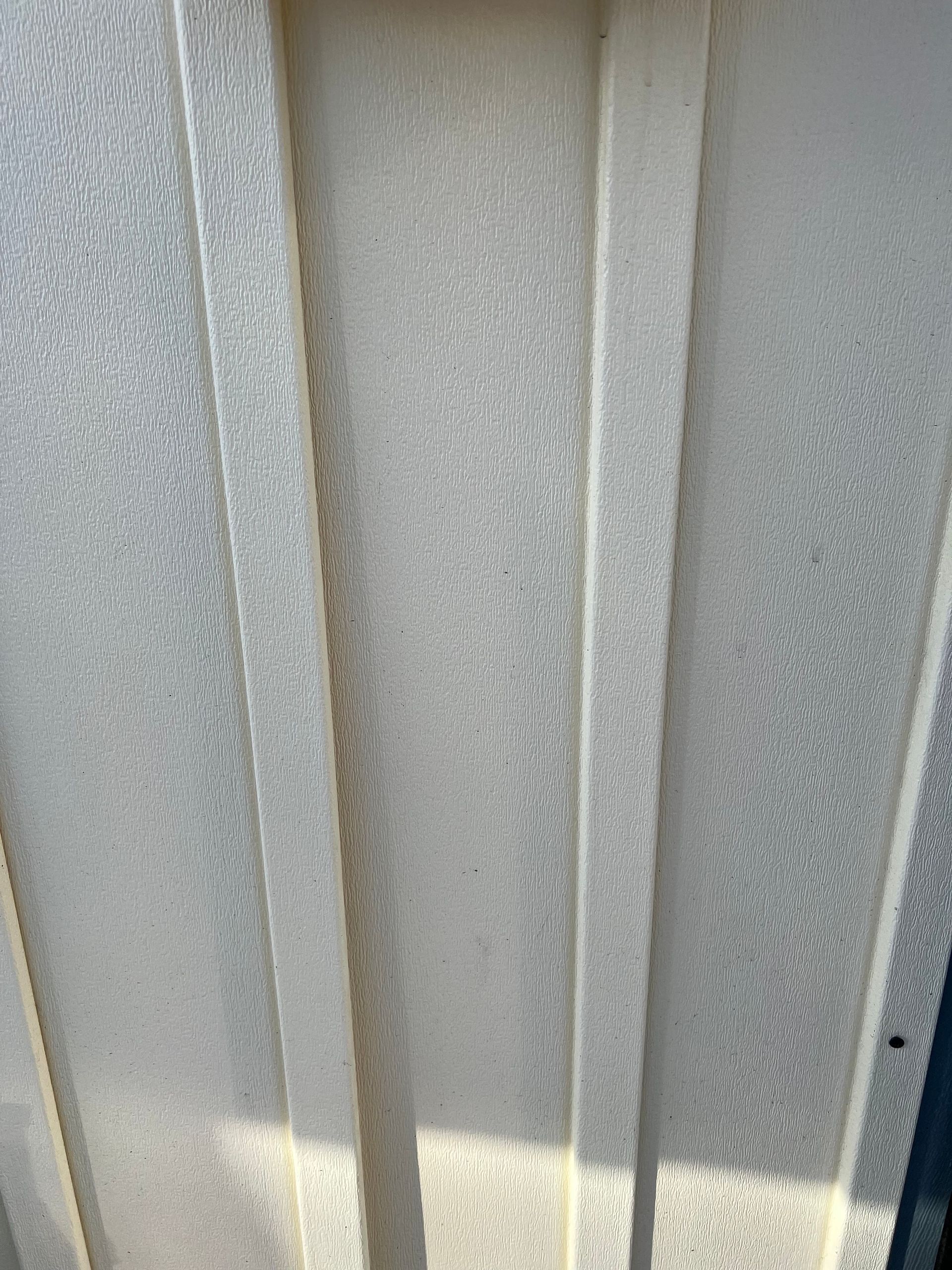 A close-up view of light-colored, textured vinyl or plastic siding panels with vertical grooves.