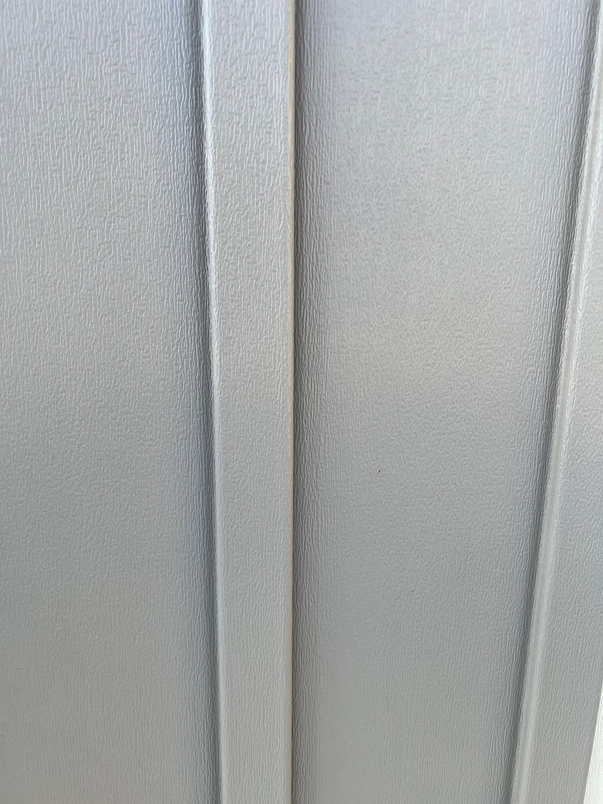 A close-up view of a grey-toned siding surface featuring vertical panels and a textured, matte finish.