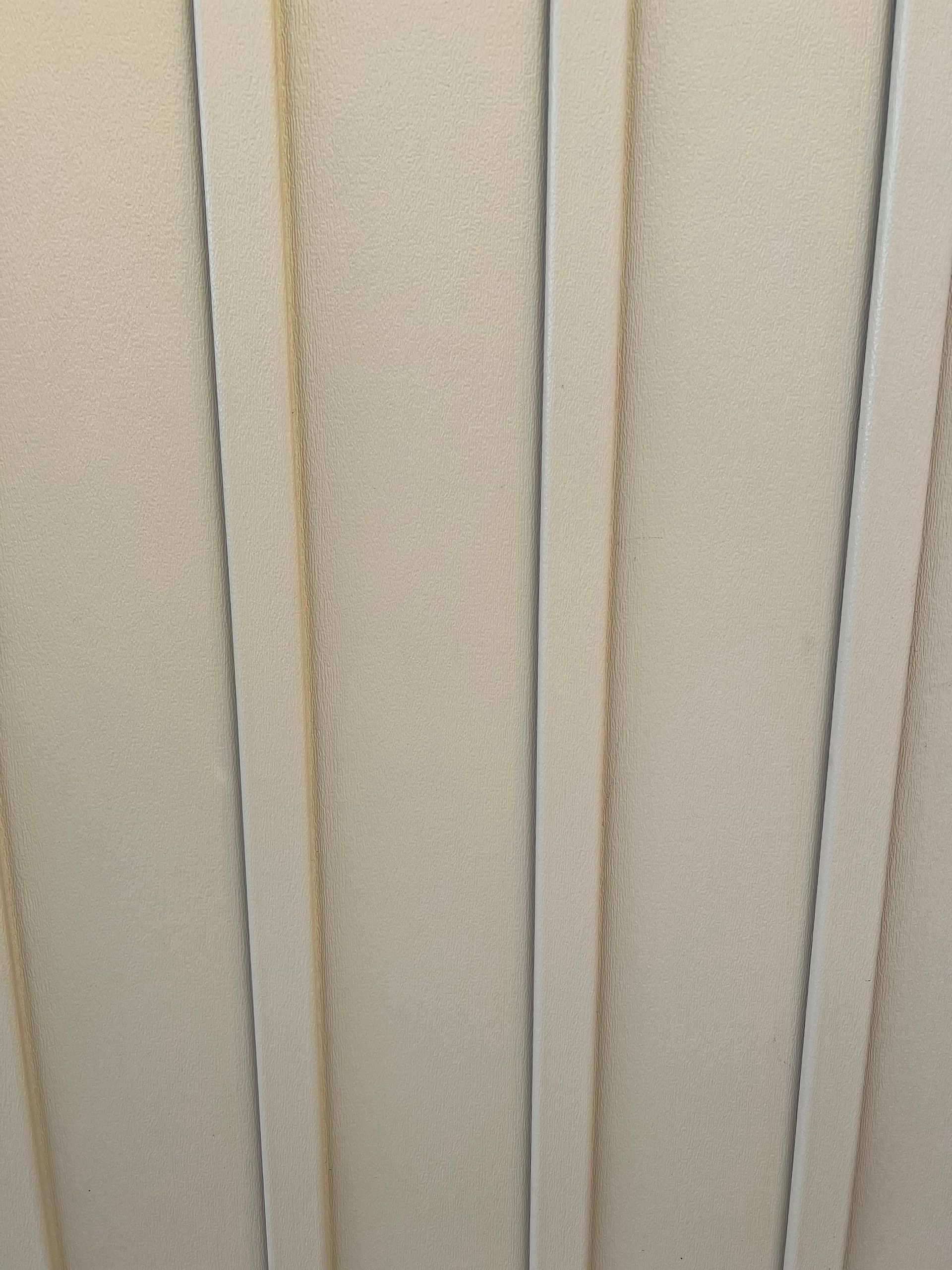 A close-up of vertical, light-colored siding panels with consistent spacing between each ridge.
