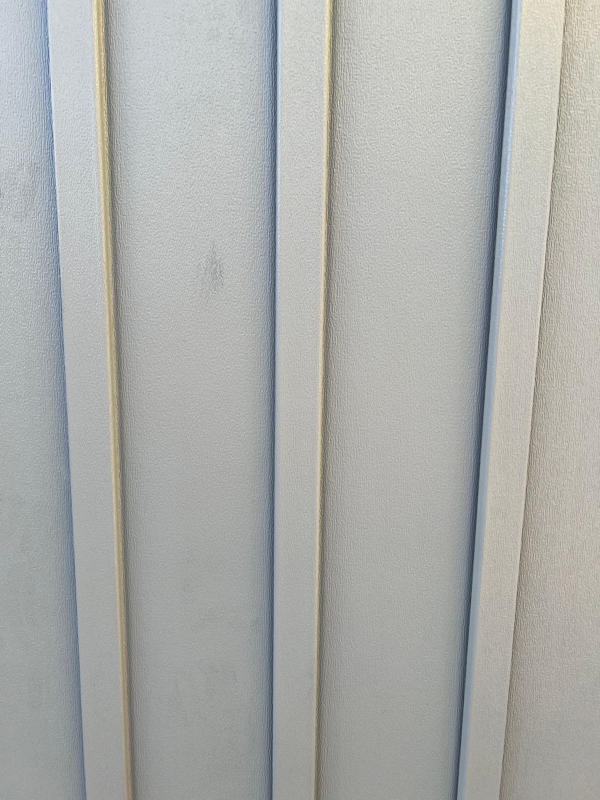 Vertical rows of textured, pale gray siding panel.