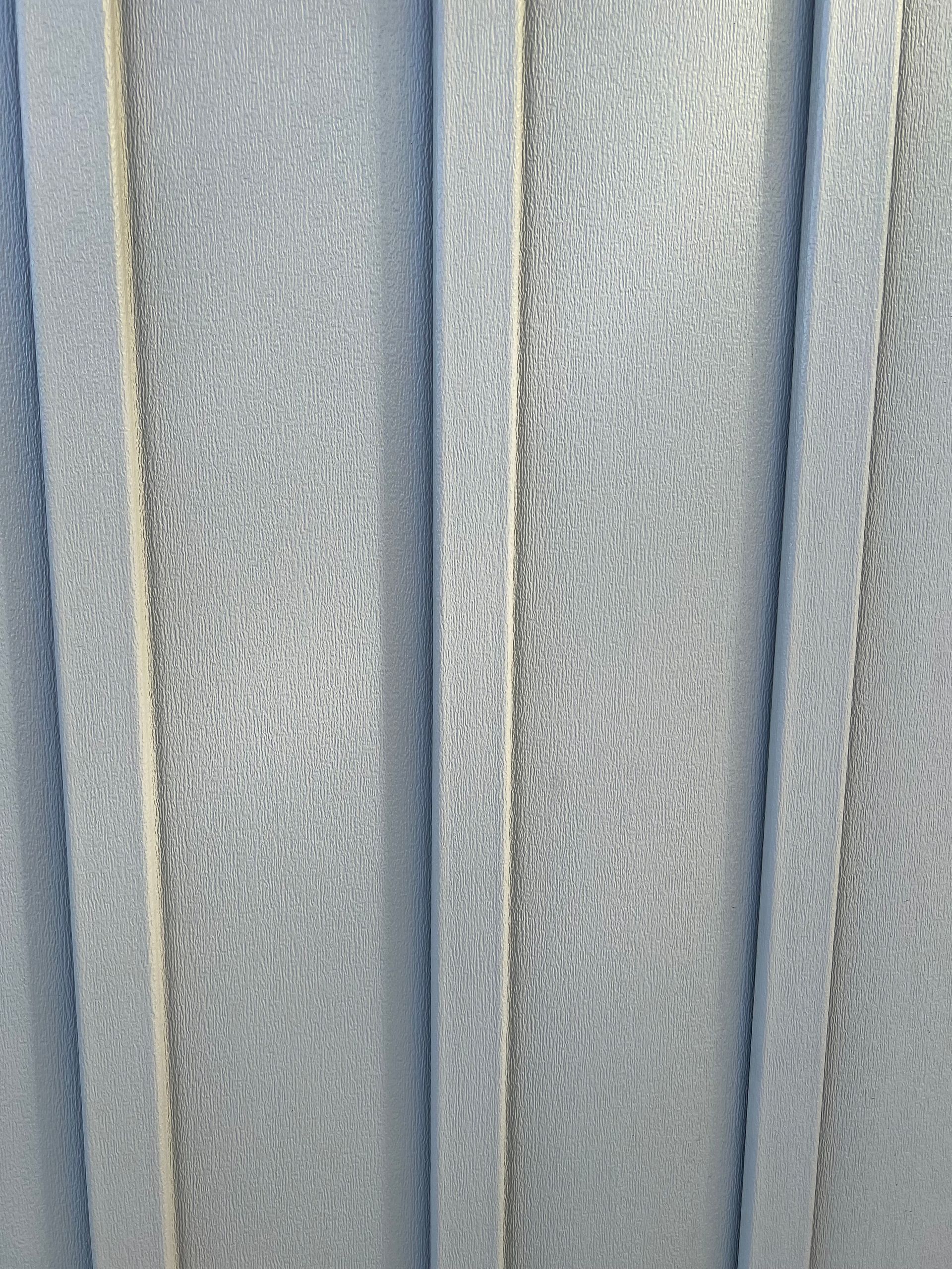 Close-up of a siding surface with vertical corrugated ridges and a textured, metallic grey finish.
