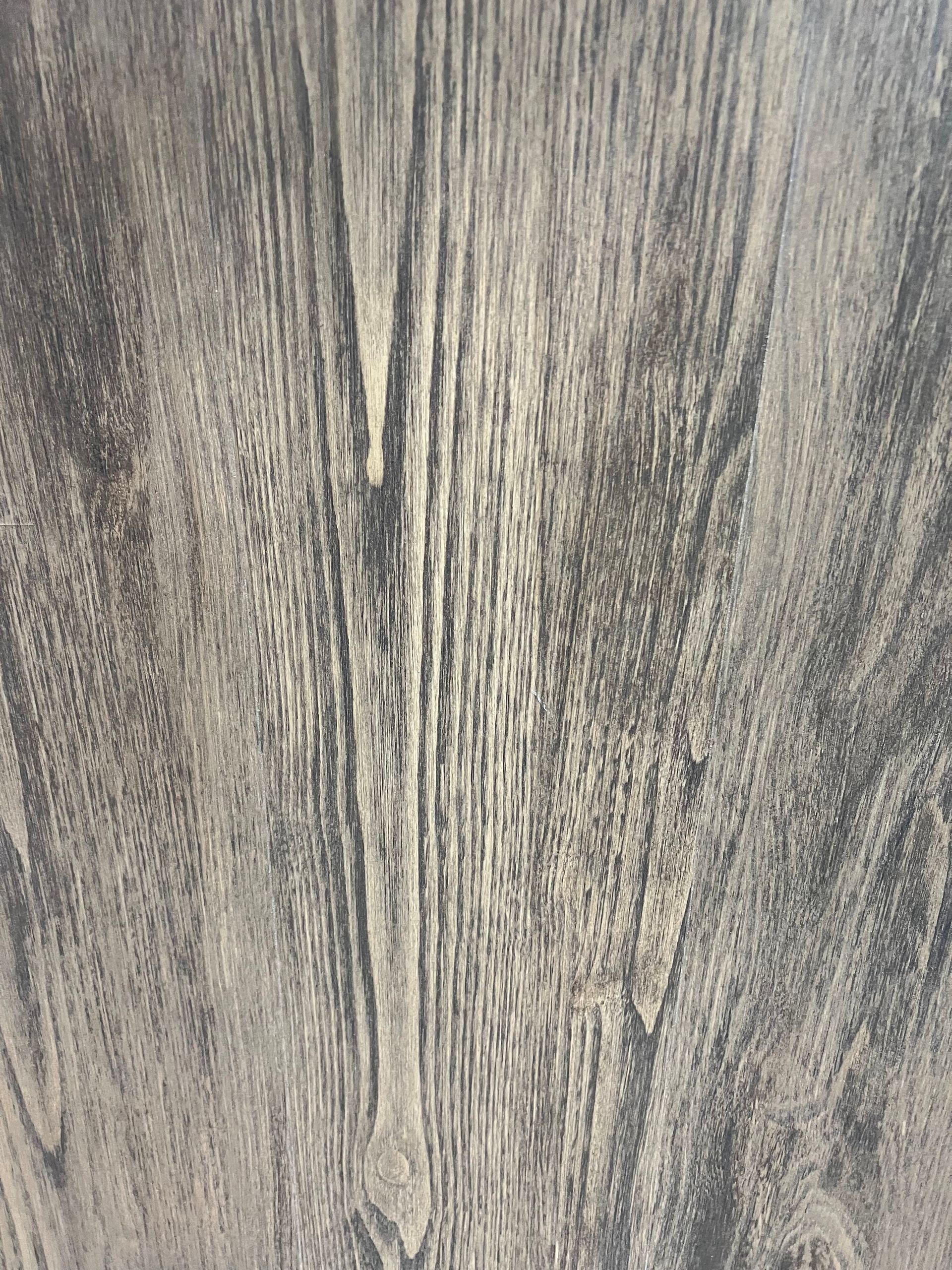 A close-up view of a light-gray wood grain pattern with vertical streaks of darker charcoal texture throughout.
