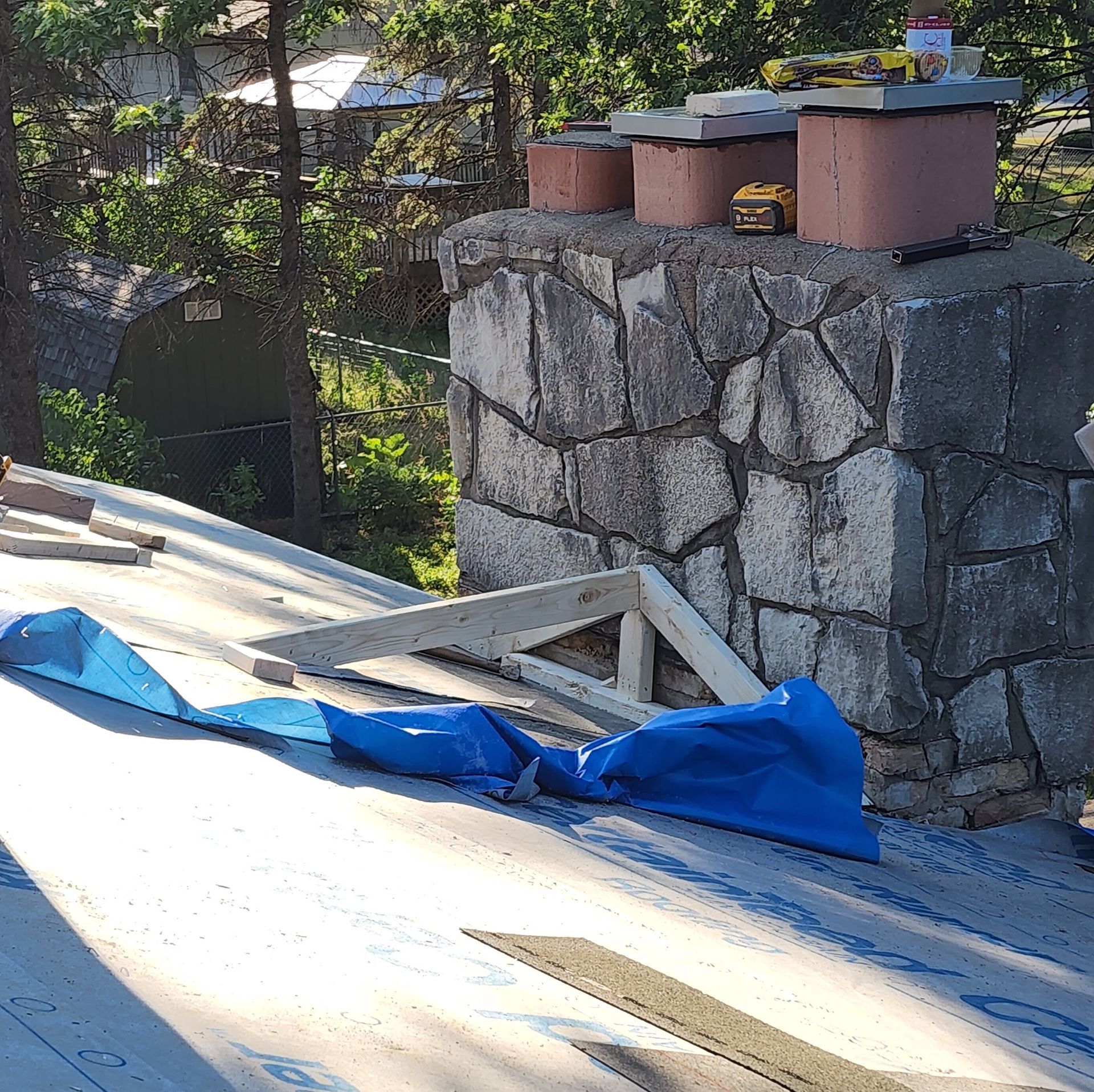 A blue tarp is laying on a roof next to a stone chimney.