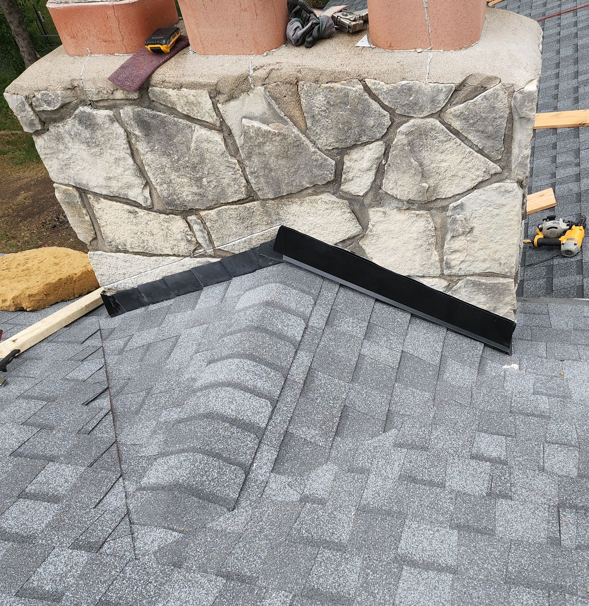 A chimney is being installed on a roof next to a stone wall.