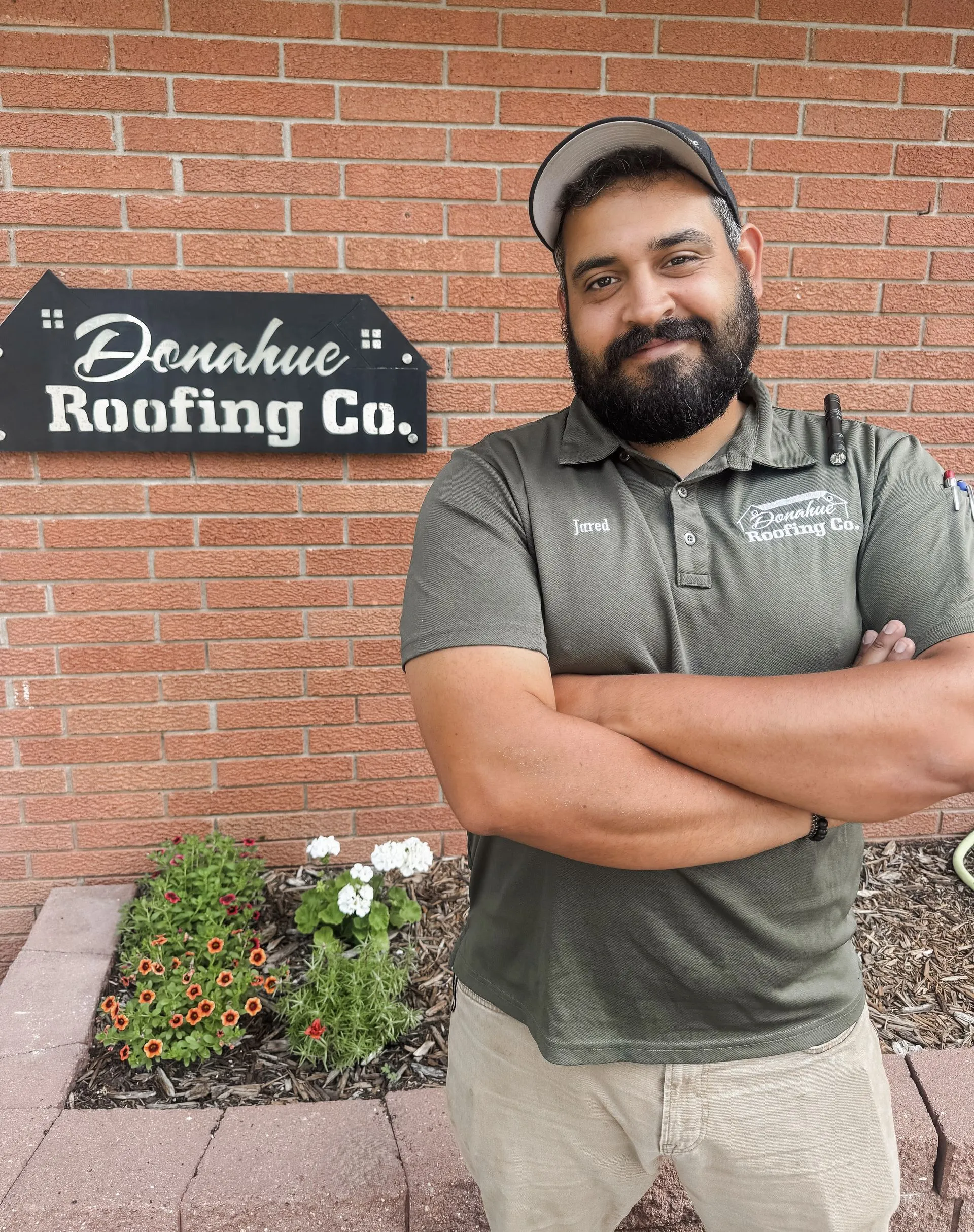 Man with crossed arms standing in front of a brick building with a