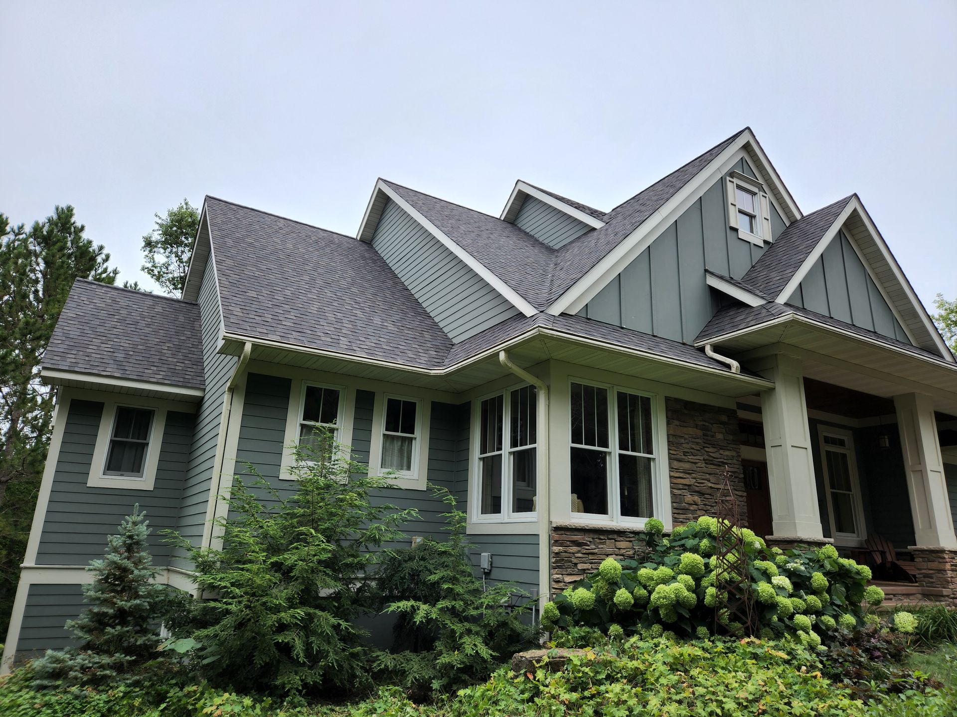 A large house with a gray roof is surrounded by trees and bushes.