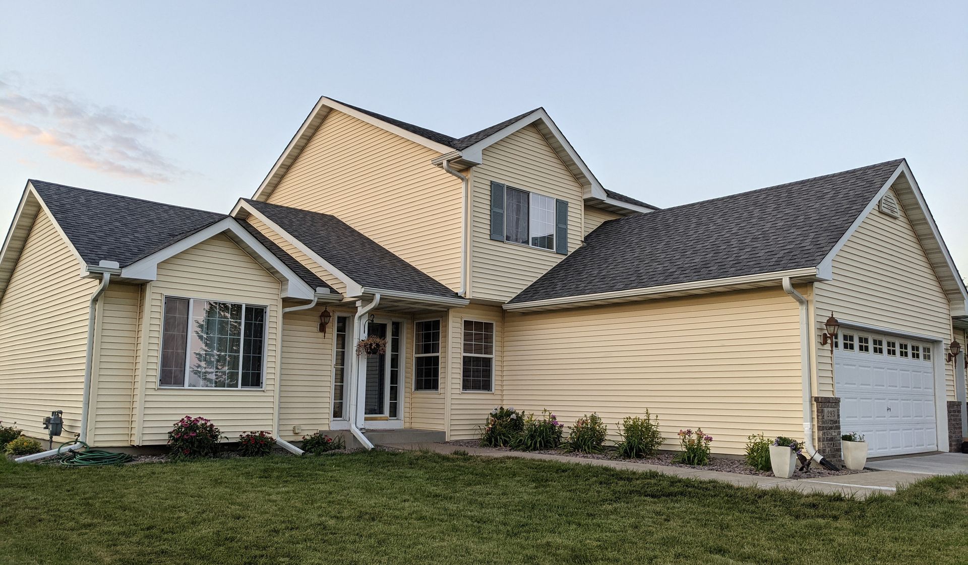 A large house with a gray roof is sitting on top of a lush green field.