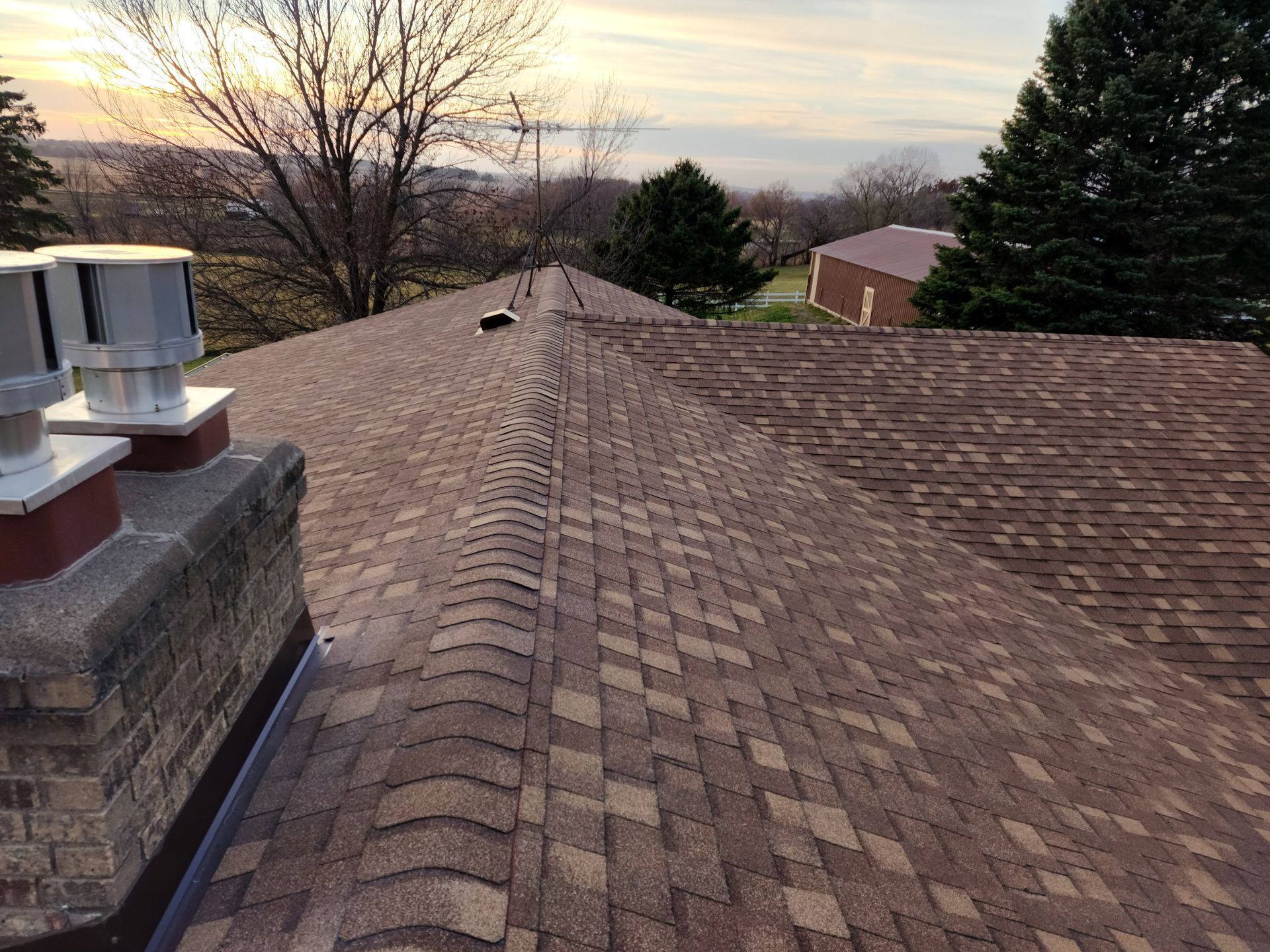 A roof with a chimney on it and a sunset in the background.
