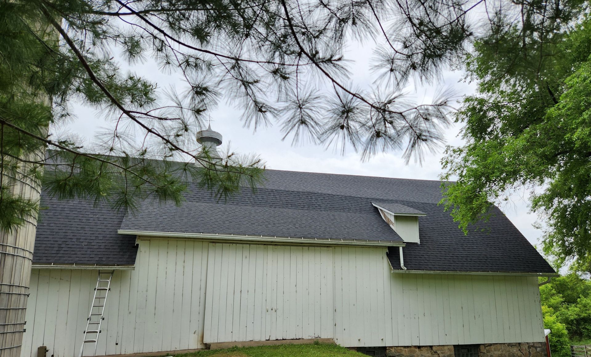 A white barn with a black roof is surrounded by trees.