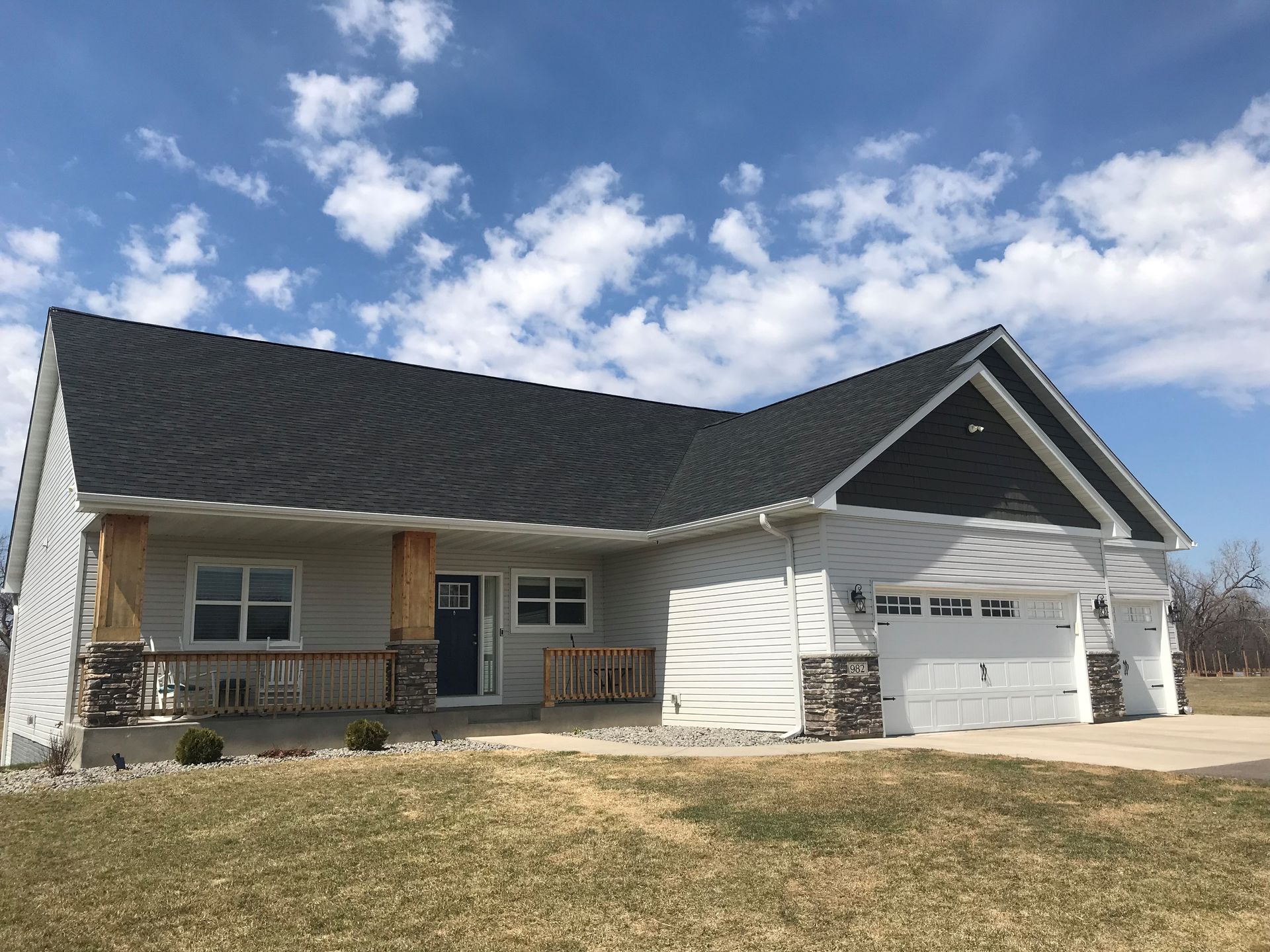 A white house with a black roof is sitting on top of a lush green field.