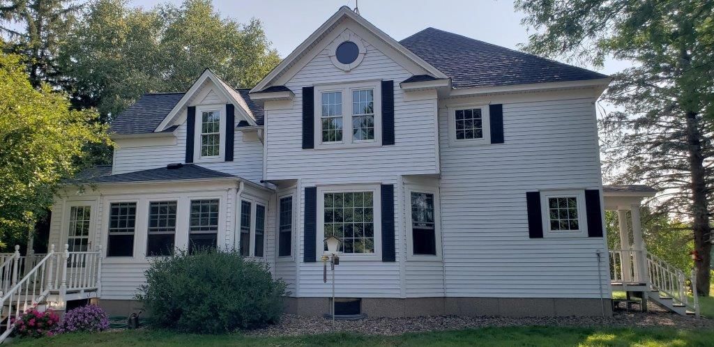 A large white house with a black roof is surrounded by trees.
