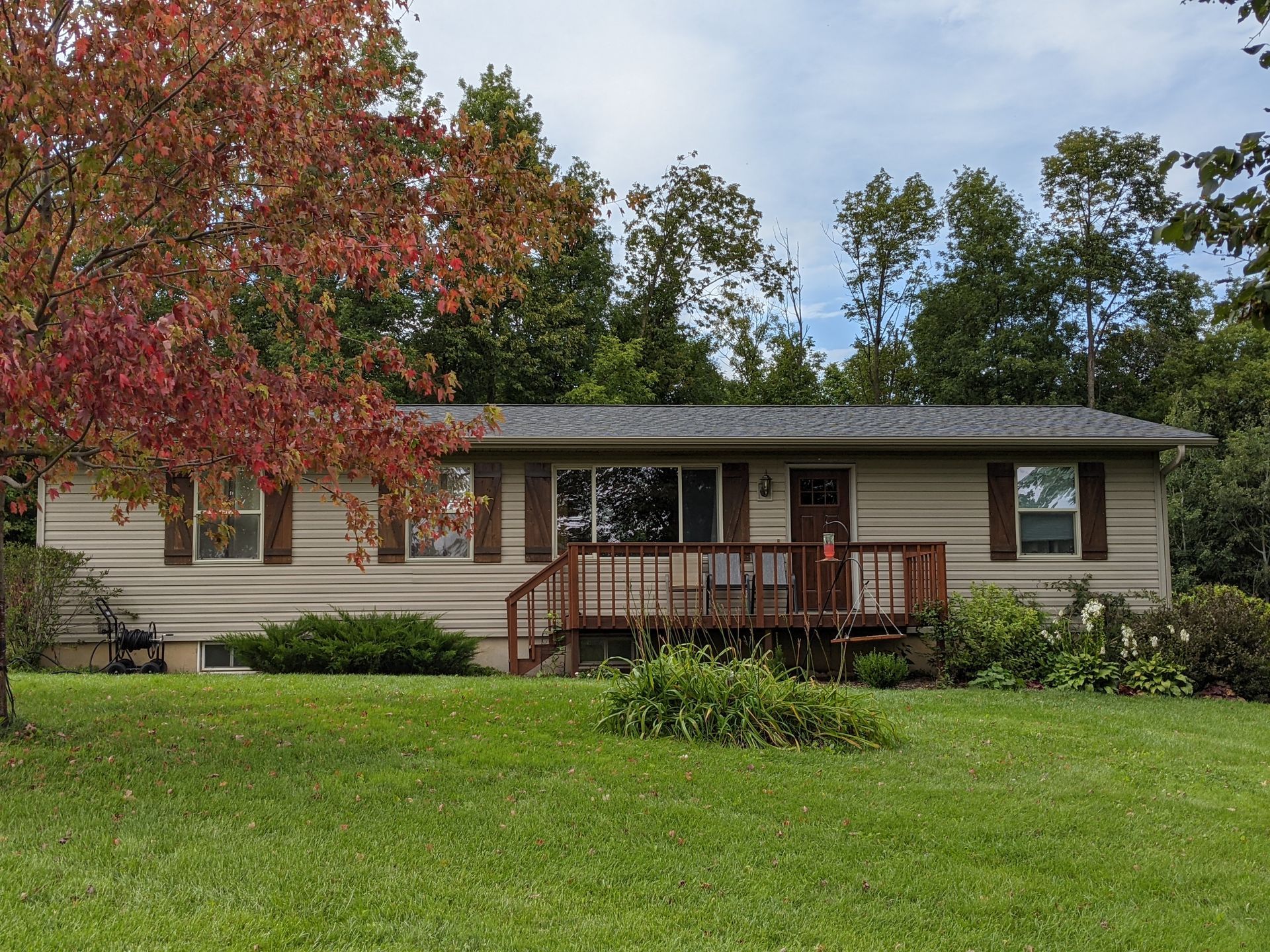 A house with a deck is sitting on top of a lush green field.