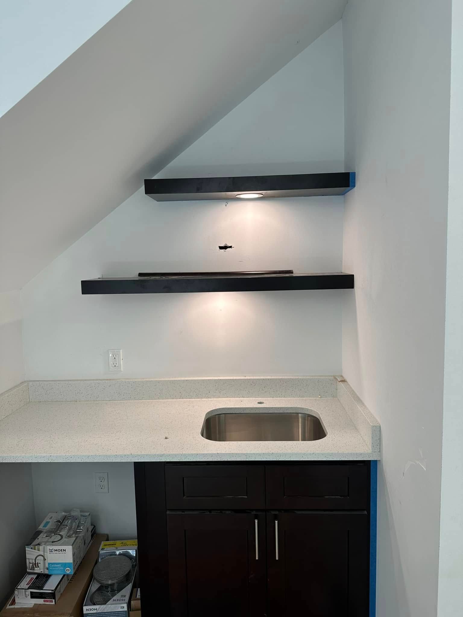 A kitchen with a sink and shelves under a staircase