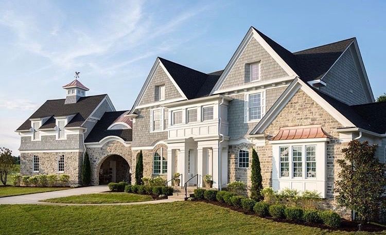 Large luxury stone house with gabled roof and landscaped lawn on a sunny day