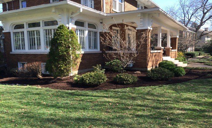 Brick house with white trim, front porch, and landscaped yard in a sunny suburban setting