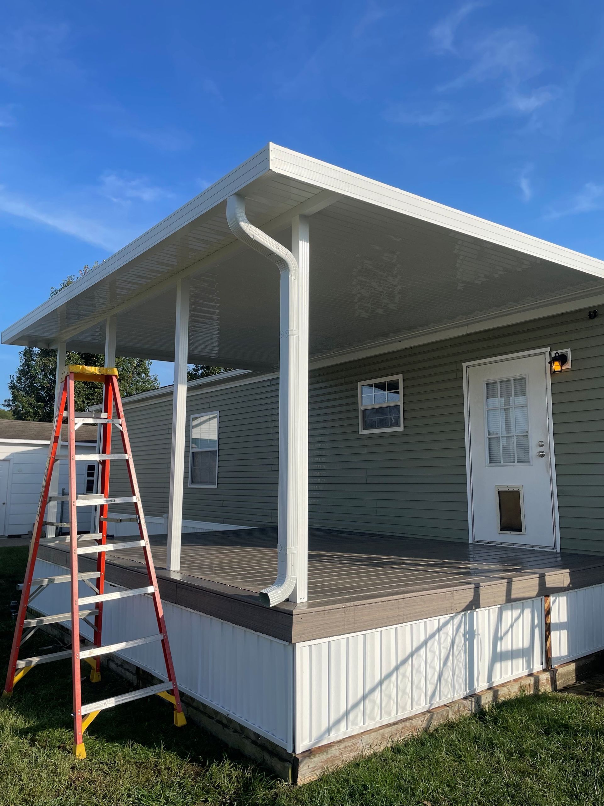 White porch with white columns, green siding, and a step ladder.
