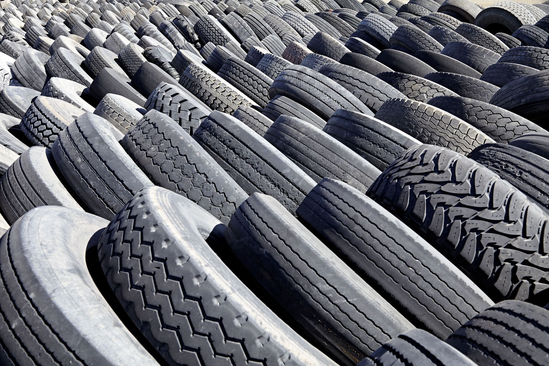 Pile of stacked used tires with visible treads in a junkyard or recycling yard