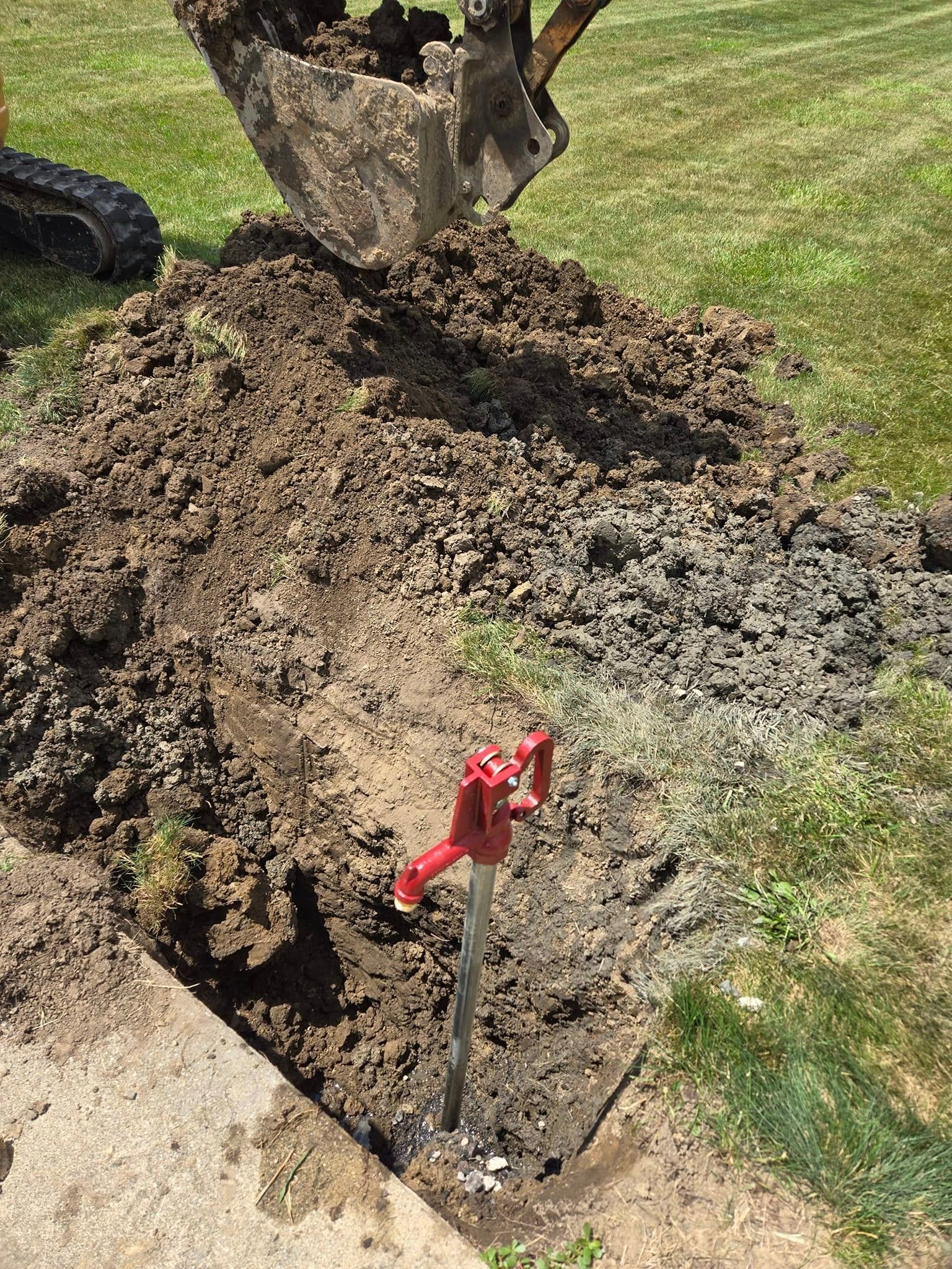 An excavator digs around a red hydrant in a grassy area.