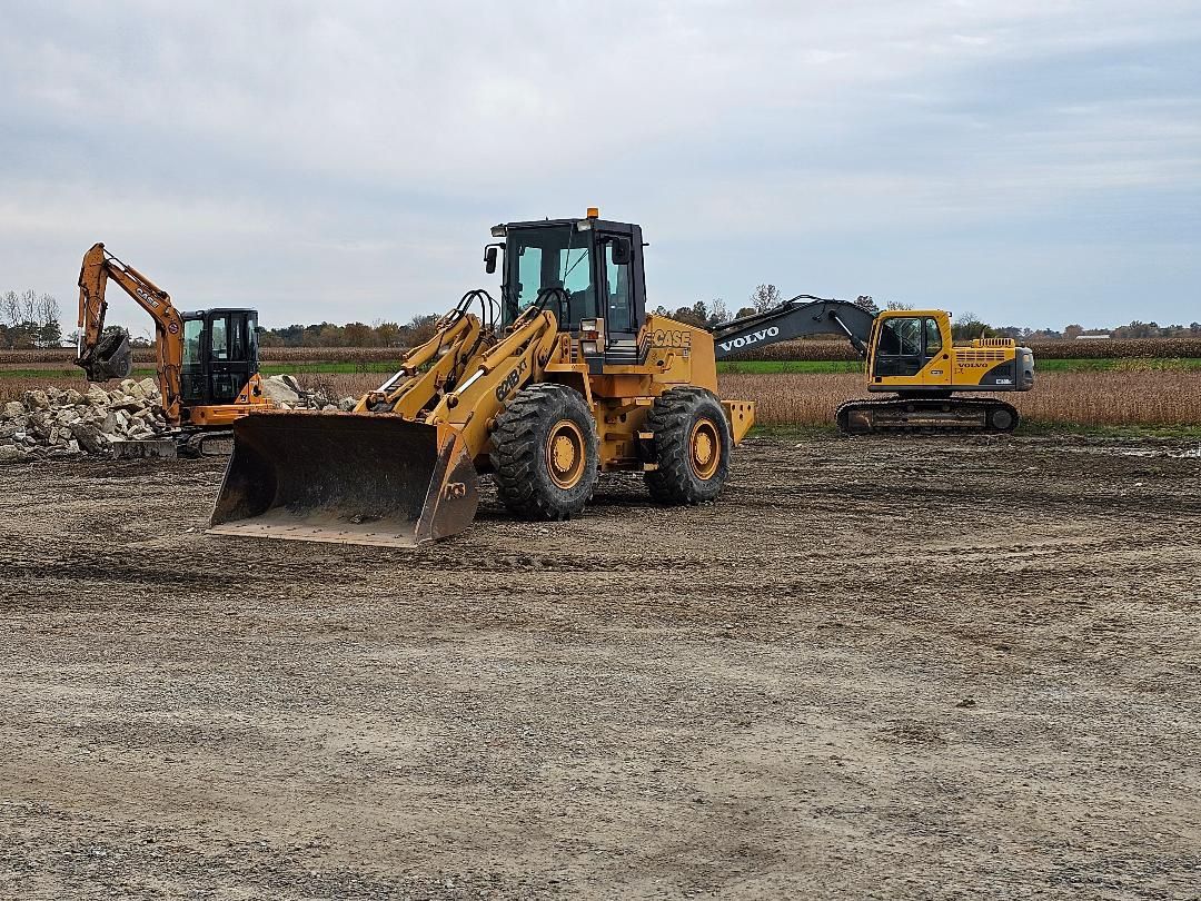Construction equipment on a muddy field under an overcast sky. Three excavators working.
