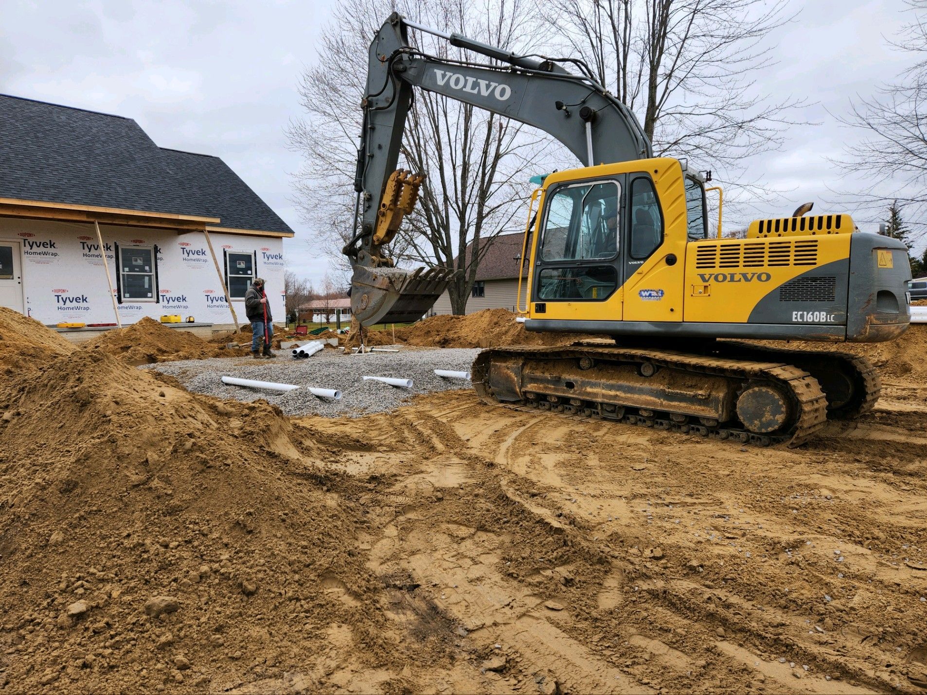 Yellow Volvo excavator on a construction site, near a house under construction.