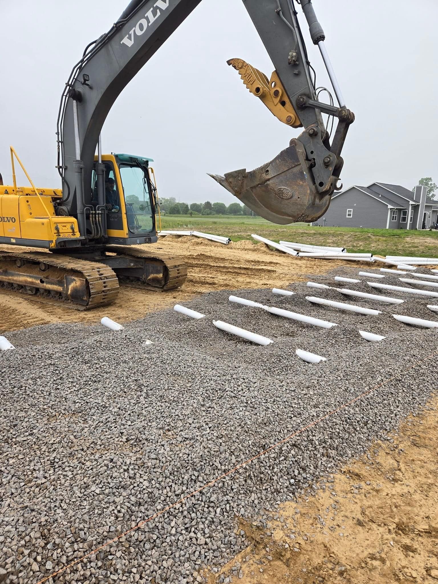 Yellow Volvo excavator placing gravel and pipes in a construction site.