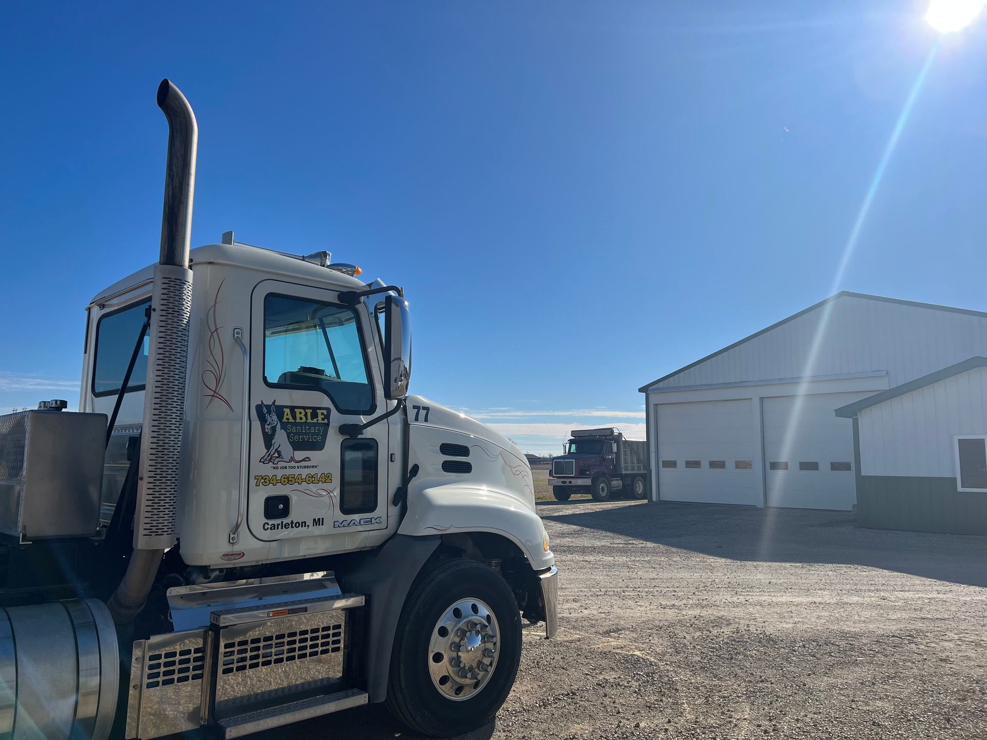 White truck parked on a gravel lot under a bright blue sky, with a garage in the background.