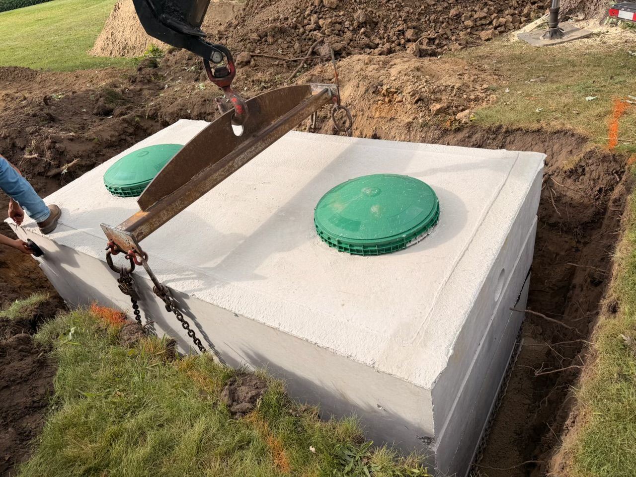 Workers installing a concrete septic tank with green lids in a grassy yard