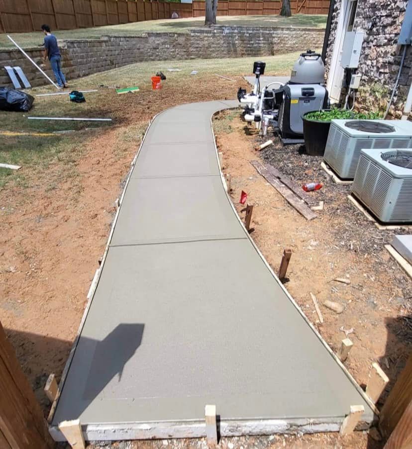 Freshly poured concrete walkway winding through a backyard construction zone.